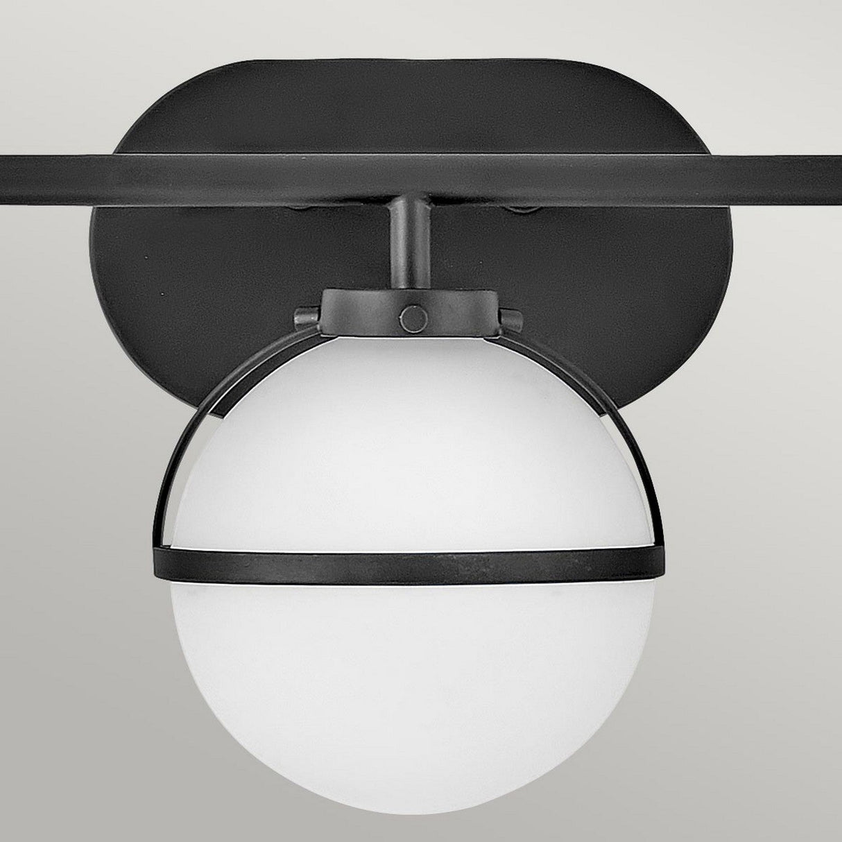 The Hollis 3 Light Wall Light - Black With Opal Glass showcases modern design through its elegant black and white features. A circular opal glass shade is enclosed within a black metal frame featuring a rectangular base, seamlessly mounting onto a light gray ceiling to combine minimalist aesthetics with vintage appeal.