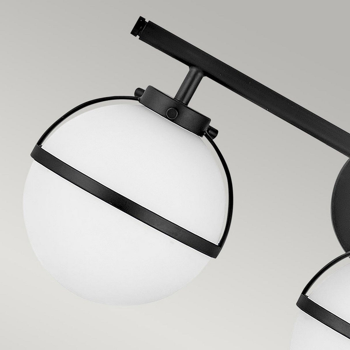 The Hollis 3 Light Wall Light - Black With Opal Glass showcases a modern spherical design with an opal globe encased in a black metal frame, mounted on a dark horizontal rod. It seamlessly combines contemporary aesthetics with vintage charm against a neutral backdrop.