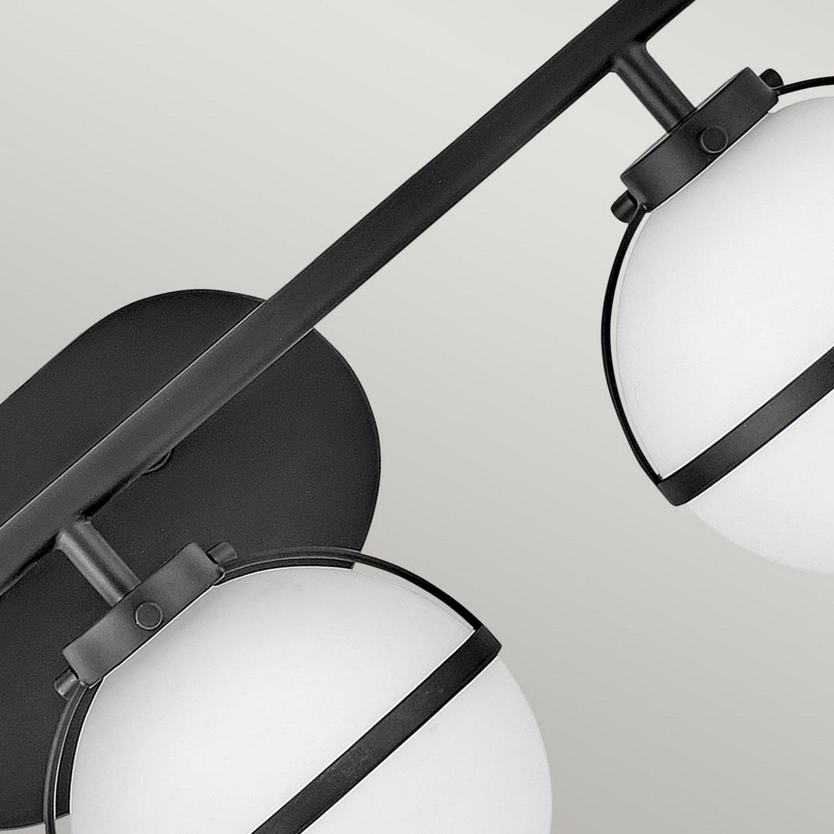 A close-up of the Hollis 3 Light Wall Light showcases its modern black design, featuring opal glass with two spherical white shades against a neutral backdrop. This fixture embodies contemporary style with sleek lines and minimalist aesthetics, seamlessly merging vintage charm with modern elegance.