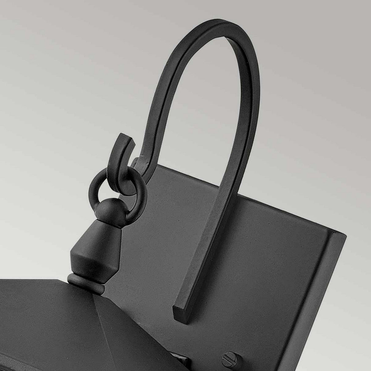Close-up of the Huntersfield Outdoor 1 Light Small Wall Lantern in black, showcasing its black finish. It features an elegantly curved, ornate arm connected to a square backplate. This simple yet sophisticated design works wonderfully as outdoor lighting. The background is plain gray.