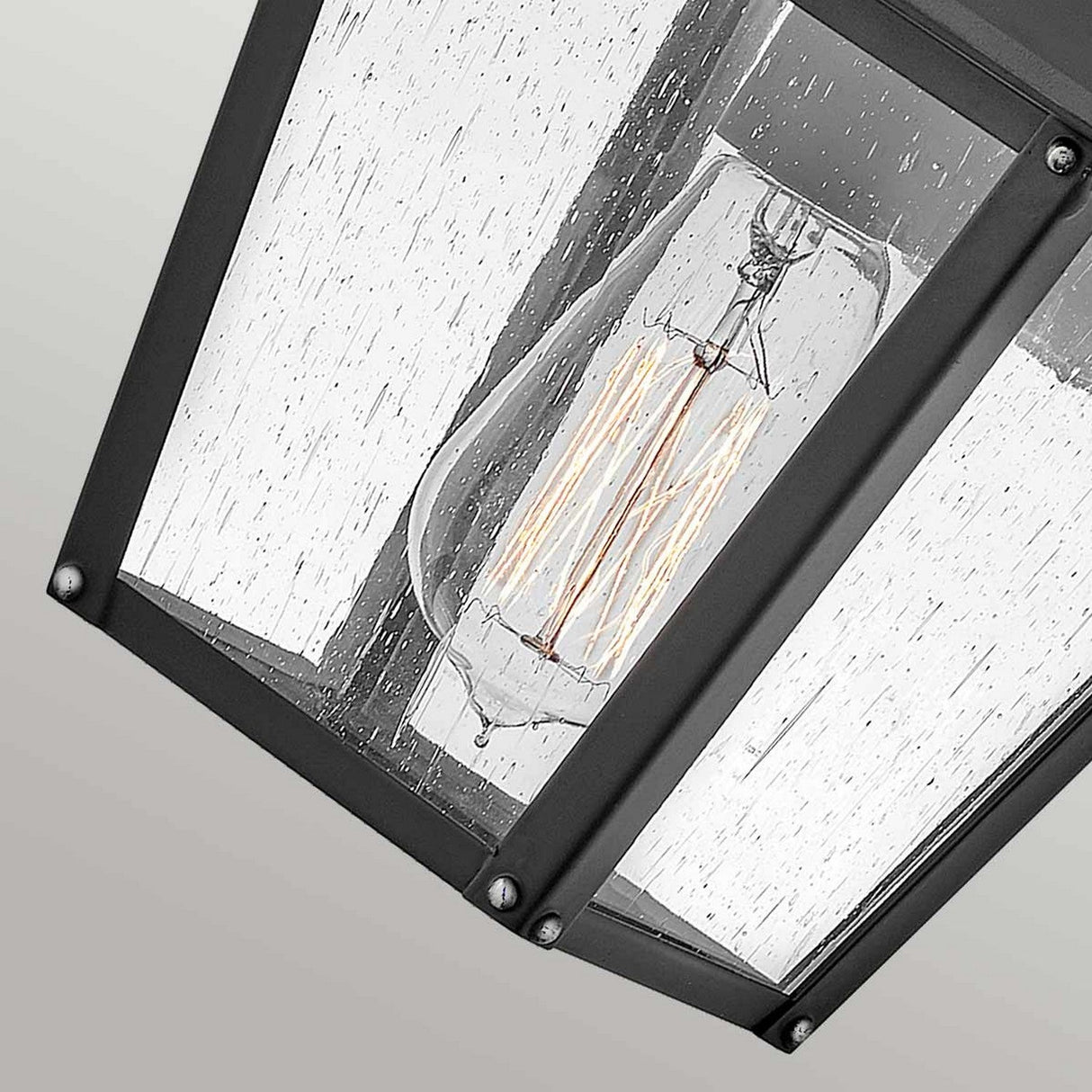 The Huntersfield Outdoor 1 Light Small Wall Lantern in black showcases a pendant-style light fixture with a vintage Edison bulb. Its clear glass enclosure is adorned with a rain-like texture and is complemented by a black metal frame, delivering a modern yet rustic aesthetic that's perfect for outdoor lighting applications.