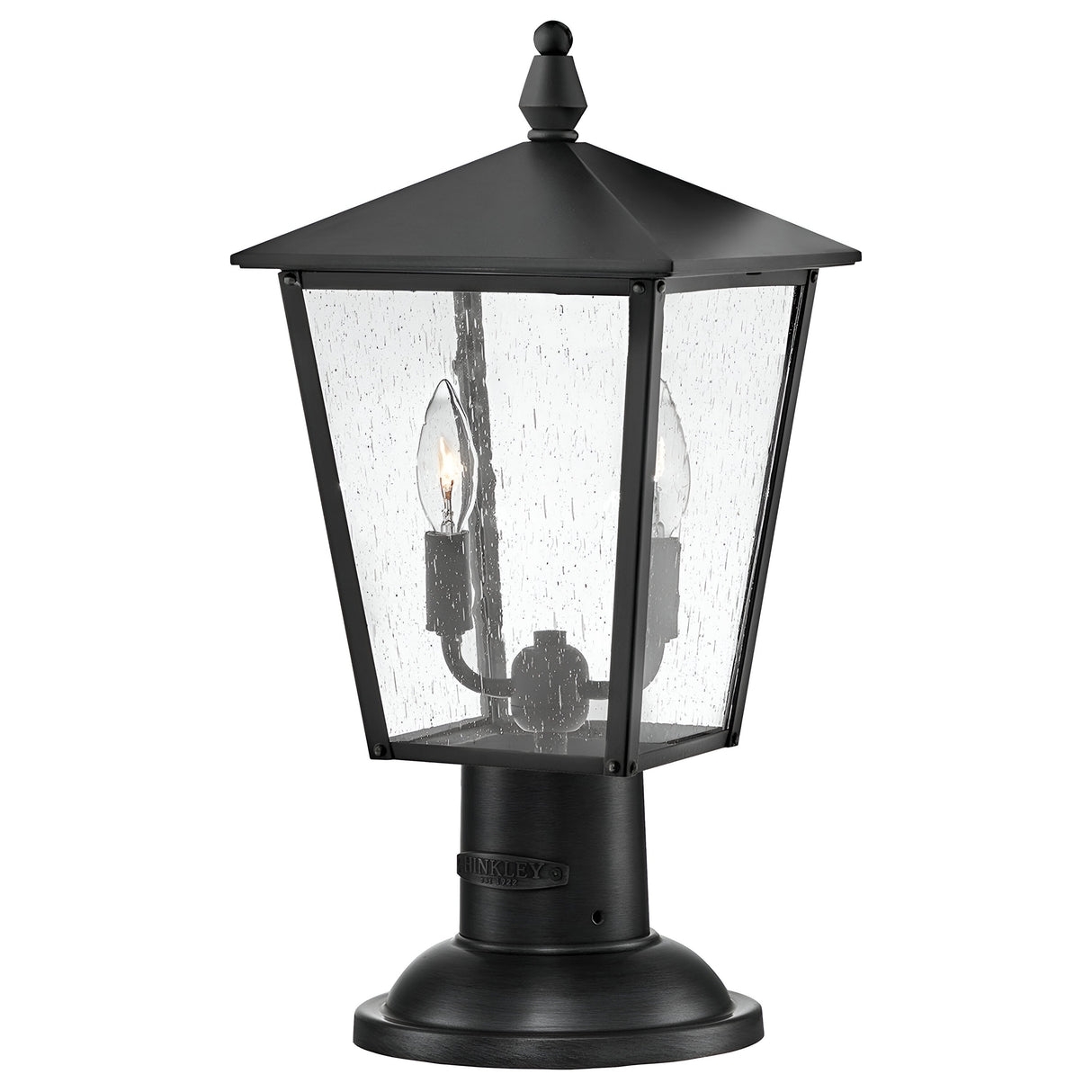 The Huntersfield Outdoor 2 Light Medium Pedestal Lantern in black showcases a classic design with a tapered square shape and clear glass panels. It is IP44 rated, featuring two candle-style bulbs inside, and the textured glass has a raindrop-like pattern. Its medium pedestal base provides both sturdiness and elegance.