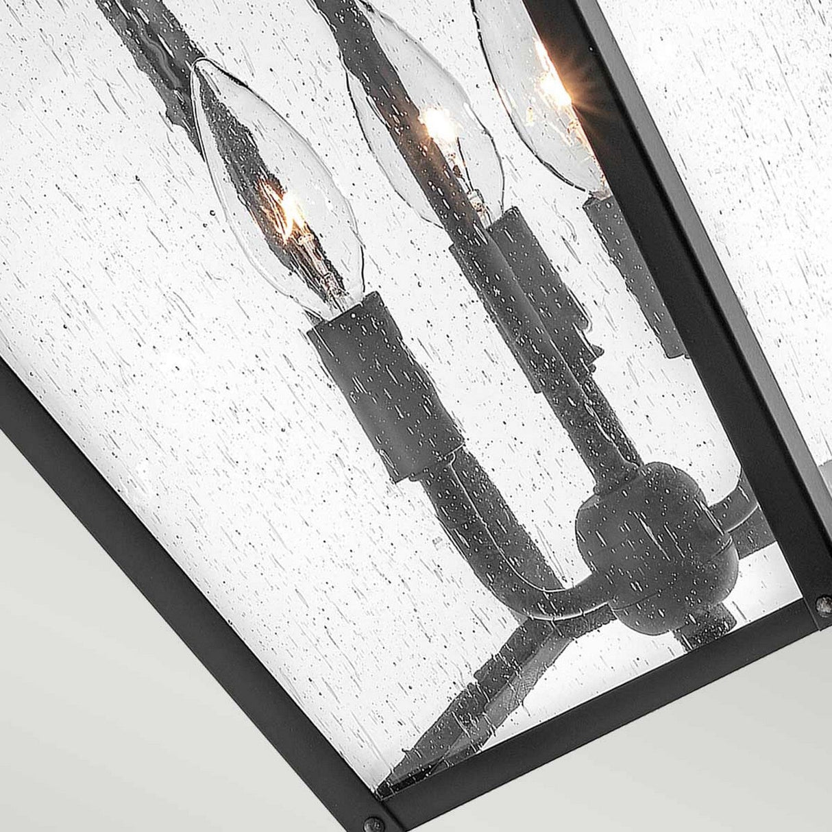 Close-up of the Huntersfield Outdoor 3 Light Large Chain Pendant in black, featuring a metal frame and clear glass panels with a raindrop-like texture. This lantern showcases a three-light design with candelabra-style bulbs inside.