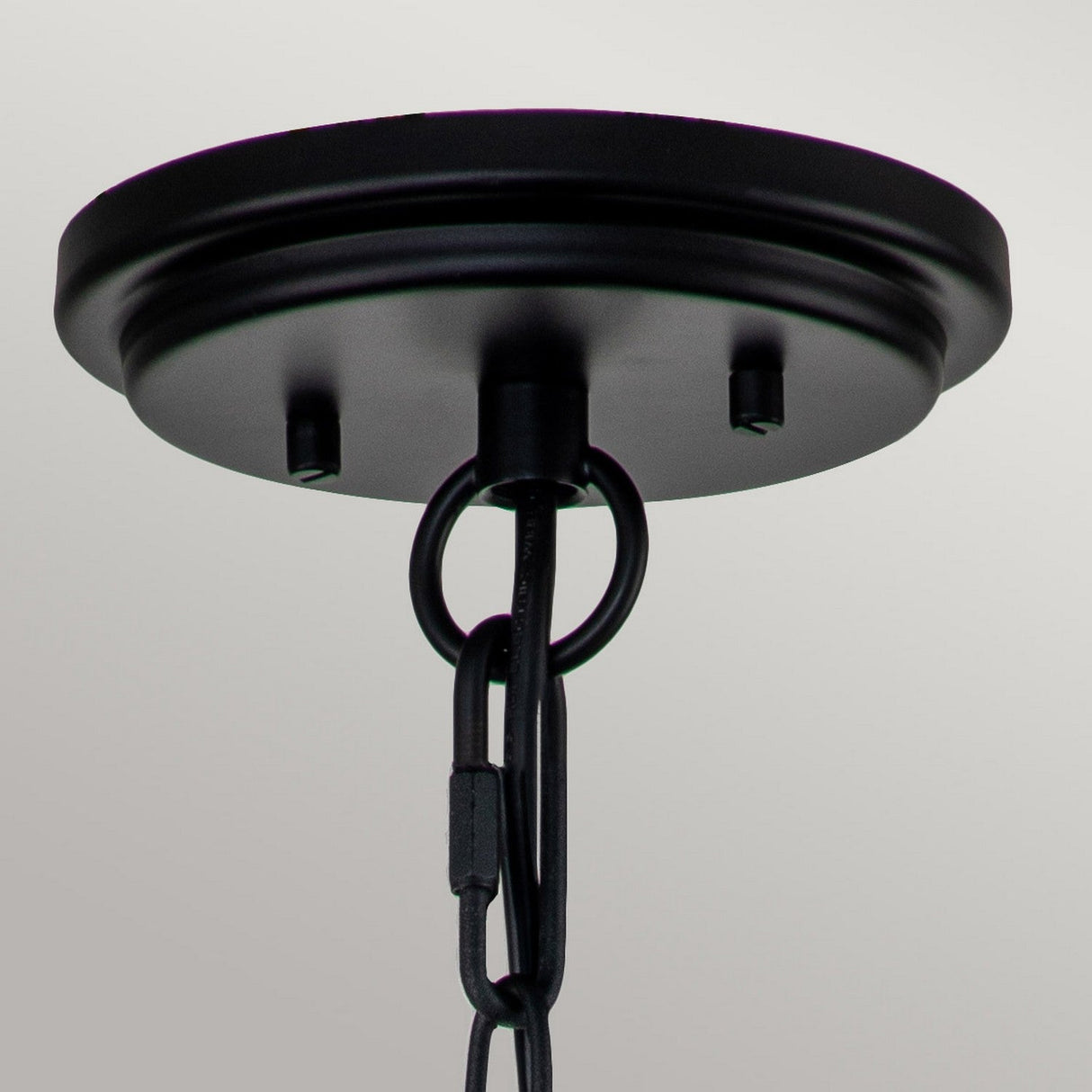 The Huntersfield Outdoor 1 Light Small Chain Pendant in Black features a close-up view of its circular base ceiling fixture. A chain hangs gracefully from the center, supported by a round hook. The clear seeded glass brings traditional charm to its simple, modern design, effortlessly blending minimalist aesthetics with classic elegance.