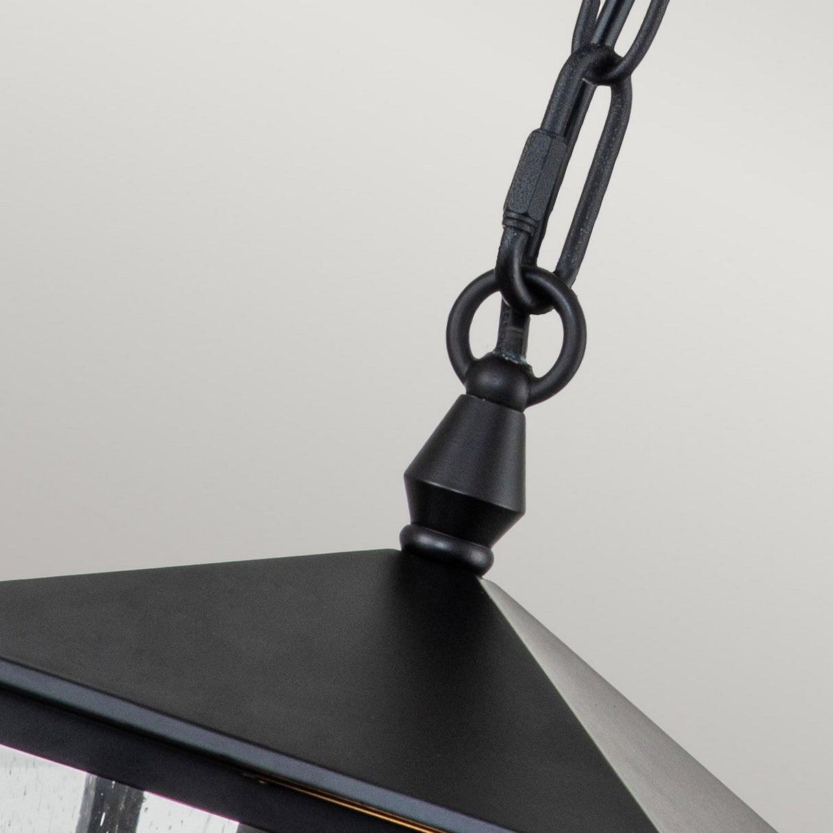 The Huntersfield Outdoor 1 Light Small Chain Pendant in black boasts a sleek, modern design with a hint of traditional charm. It includes a chain with a loop connection at the top that attaches to a pyramid-shaped shade, while the plain gray background highlights its minimalist style.
