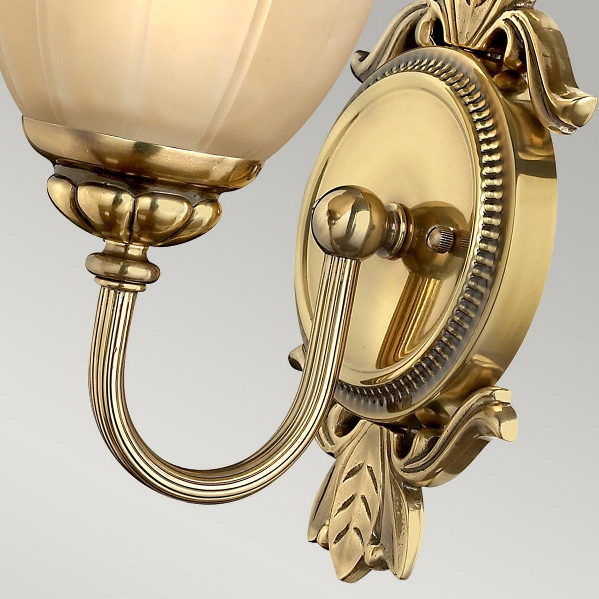 A close-up of the Isabella 1 Light Wall Light showcases its elegant design, featuring a marbled etched amber glass lampshade and intricate details such as leaf motifs and a circular backplate. The burnished brass finish adds a gleaming touch of sophistication.