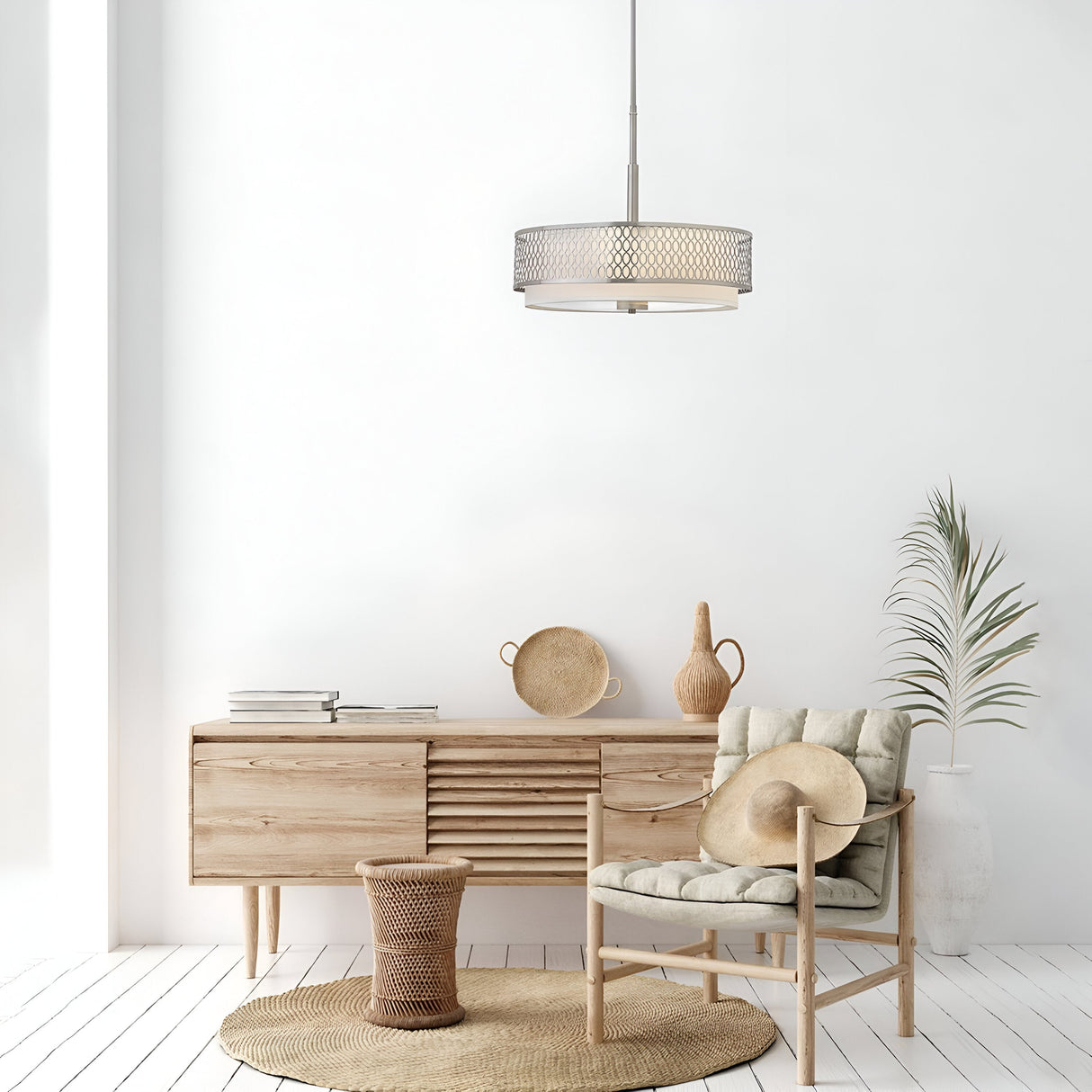 A bright, minimalist living room showcases a light wood sideboard complemented by a touch of modern elegance. The Jules 3 Light Pendant / Semi-Flush in Brushed Nickel hangs overhead, casting a warm glow over the neutral-toned decor. A chair with a cushion is positioned on a circular rug alongside a woven basket and potted plant, all set against the backdrop of a white wall.