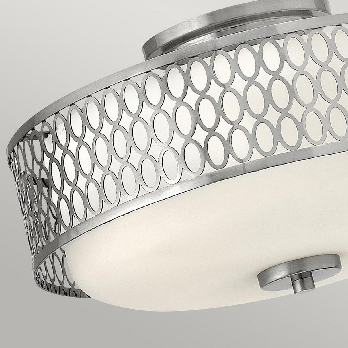 Close-up of the Jules 3 Light Flush fixture, featuring an intricate circular pattern on a metal frame in a Brushed Nickel finish surrounding a frosted glass cover, set against a neutral background.