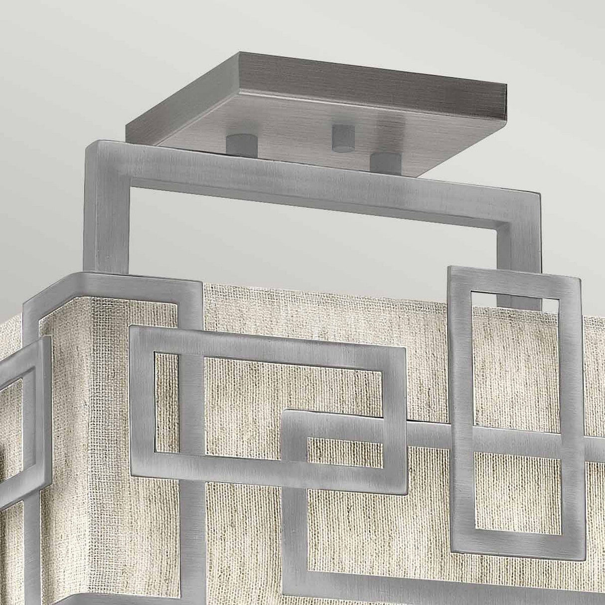 The Lanza 3 Light Semi Flush in Antique Nickel showcases modern sophistication with its interlocking rectangular metal frames. Set against a textured, light-colored fabric backdrop, the square ceiling mount enhances the contemporary decor.
