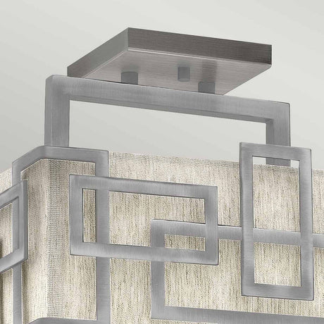 The Lanza 3 Light Semi Flush in Antique Nickel showcases modern sophistication with its interlocking rectangular metal frames. Set against a textured, light-colored fabric backdrop, the square ceiling mount enhances the contemporary decor.