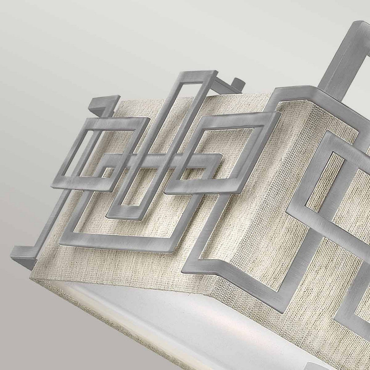 A detailed view of the Lanza 3 Light Semi Flush in Antique Nickel showcases its modern geometric design with overlapping rectangular metal elements against a beige textured background. This fixture embodies clean lines and contemporary elegance, making it an ideal choice for modern interiors.