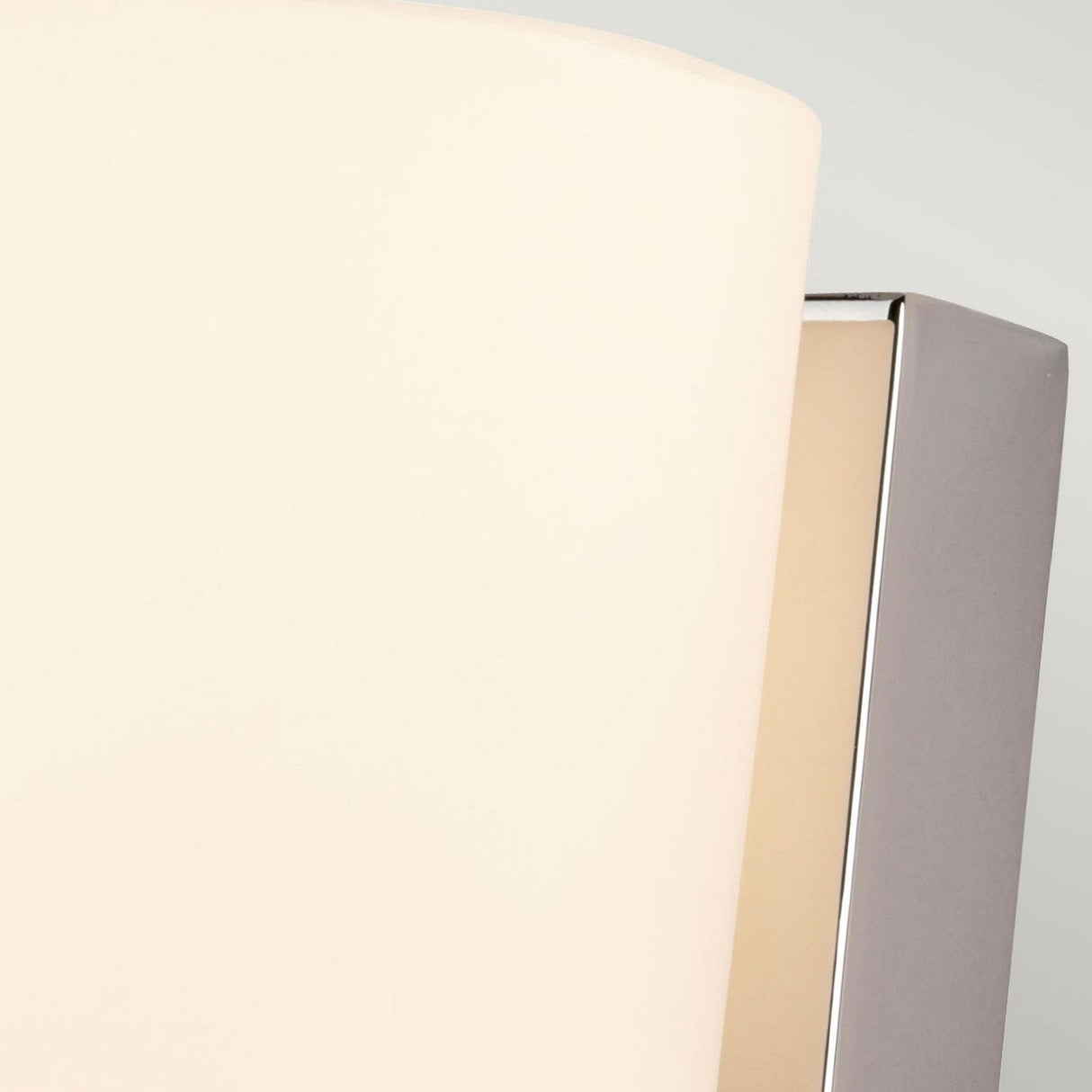 A close-up of the Lanza 1 Light Wall Light - Polished Chrome features a smooth, curved white shade paired with a polished chrome base. This design epitomizes contemporary craftsmanship and minimalism, set against a light gray background.