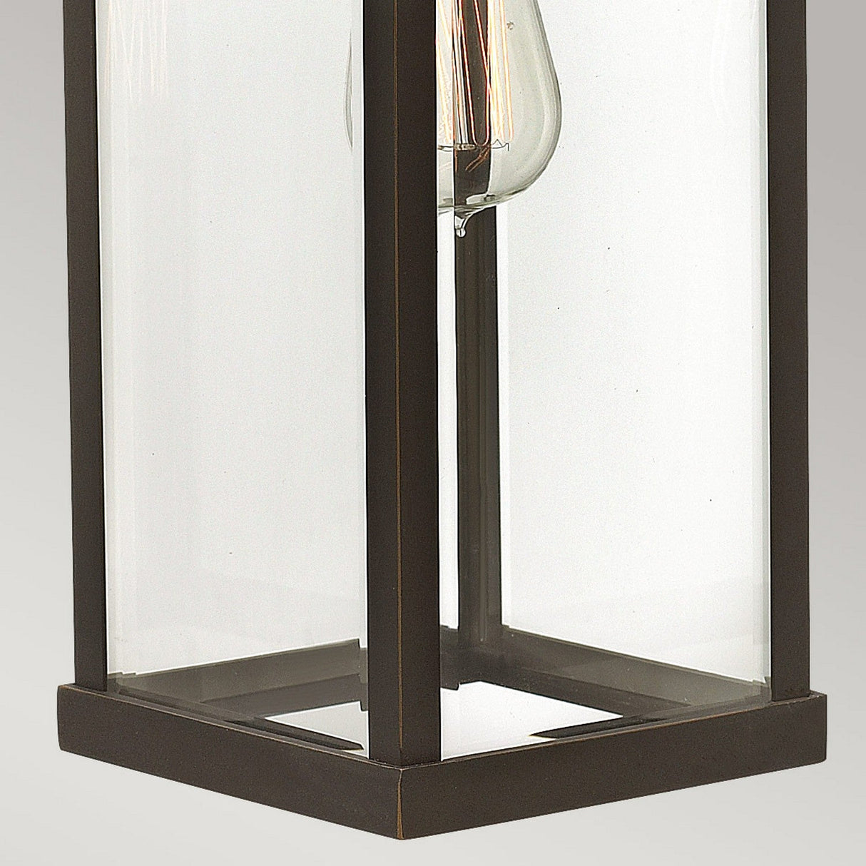 Close-up of the Manhattan Outdoor 1 Light Large Wall Lantern, highlighting its rectangular metal and glass design with a clear light bulb inside. The oil-rubbed bronze frame and transparent panels beautifully showcase its simple, modern style.