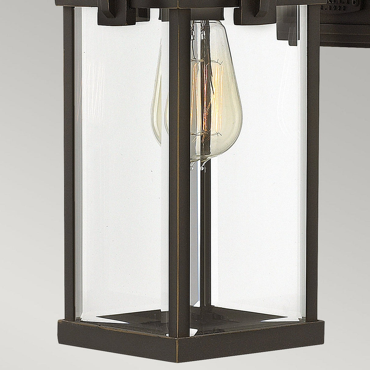 The Manhattan Outdoor 1 Light Medium Wall Lantern, featuring an oil-rubbed bronze finish and a vintage-style exposed bulb, is encased in a clear glass frame and mounted on a wall. Its softly glowing bulb accentuates its IP44 rating, bringing both style and durability to your exterior decor.