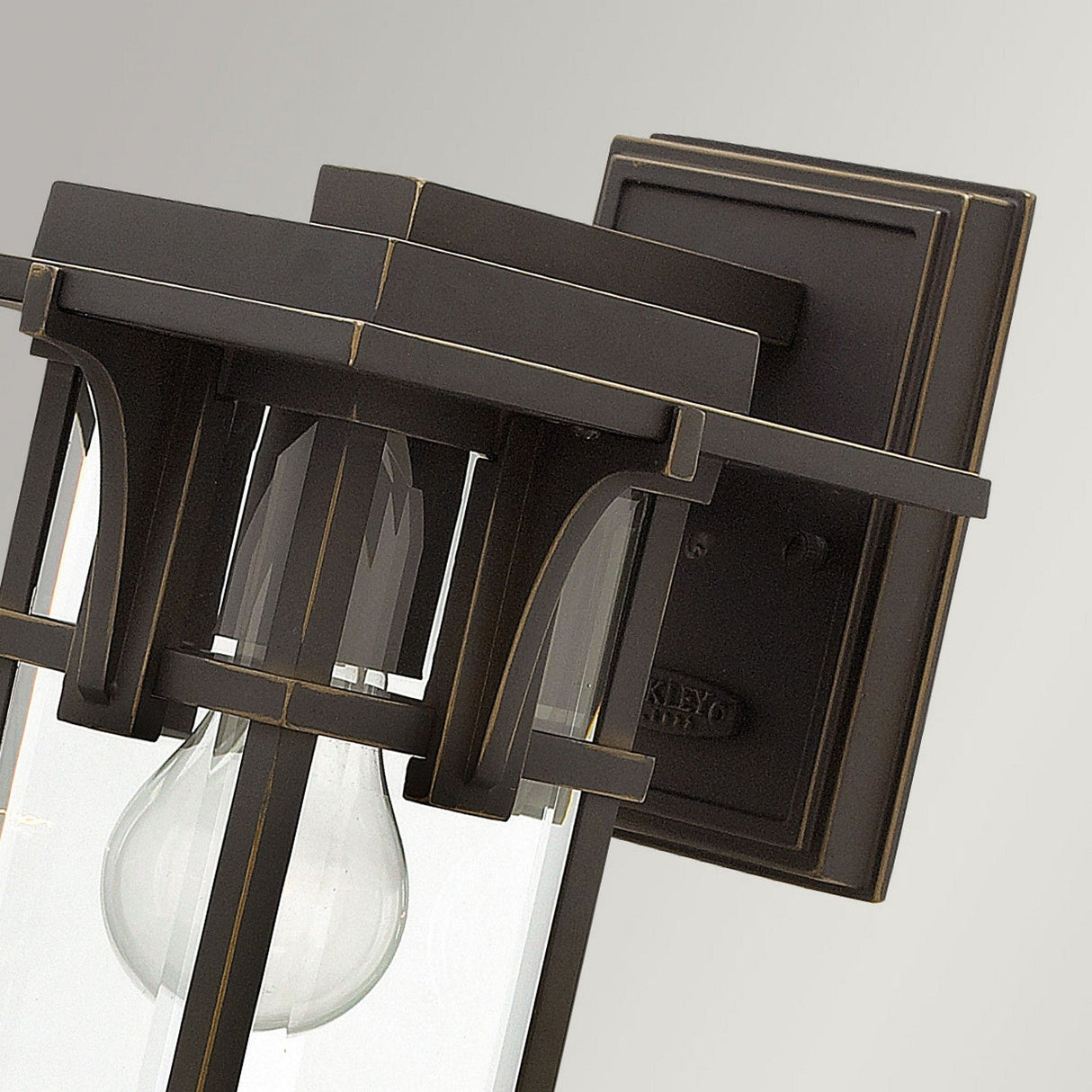 A detailed view of the Manhattan Outdoor 1 Light Small Wall Lantern reveals its vintage-inspired charm, highlighted by a beautiful oil rubbed bronze finish. The design includes a rectangular backplate and lantern-style structure with clear glass panels, elegantly showcasing the exposed light bulb inside.