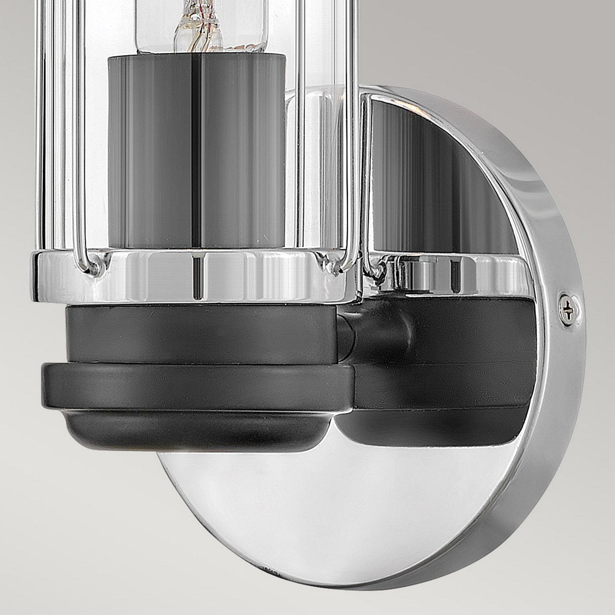 Product Description: A close-up of the Masthead 1 Light Wall Light in polished chrome and black, showcasing its modern design with a cylindrical glass shade. Ideal for bathroom décor, this fixture has a sleek black interior and is mounted on a round, reflective metal backing.