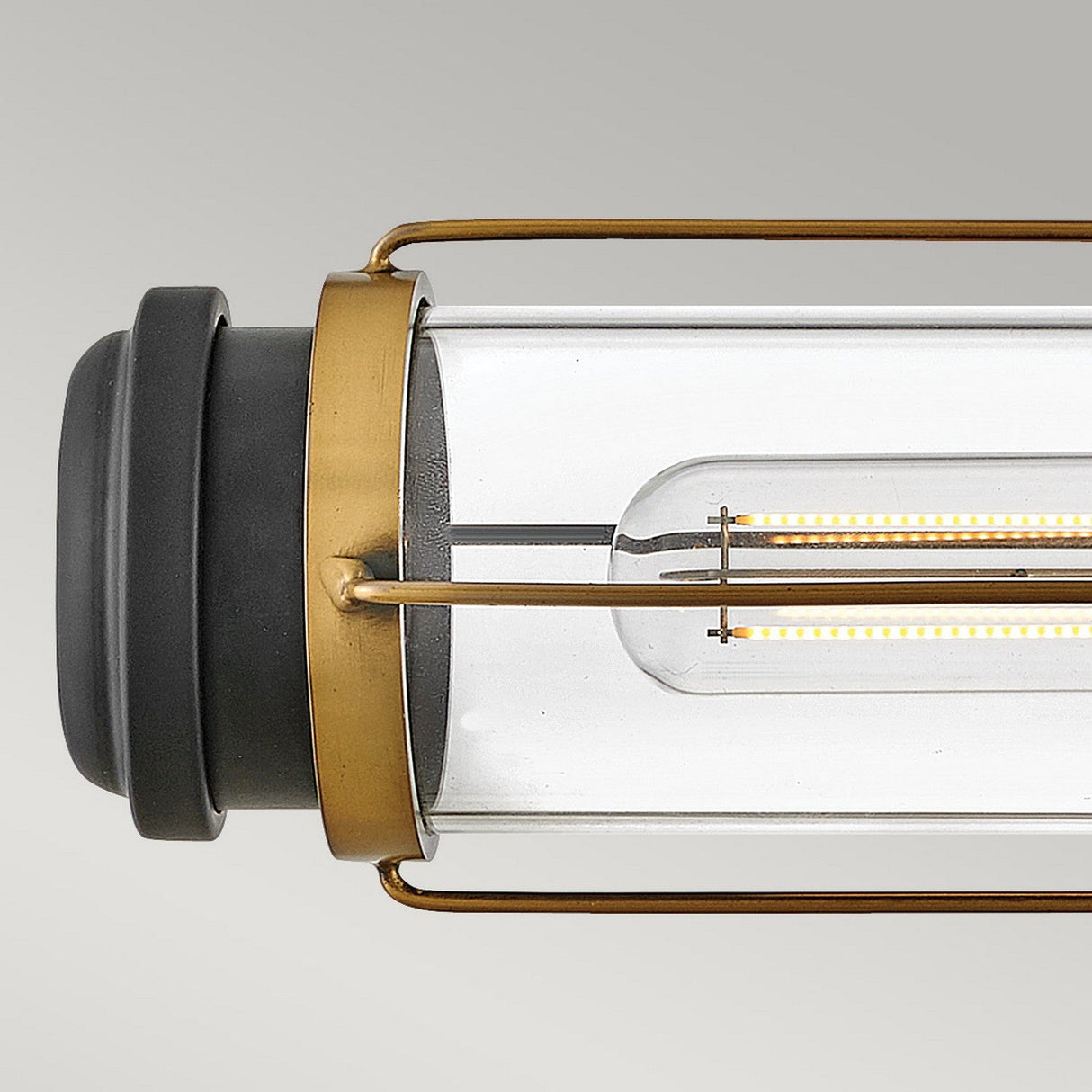 Close-up of the Masthead 2 Light Wall Light, featuring a cylindrical glass lantern with a Heritage Brass finish and black end cap. The clear glass shades showcase a visible LED filament inside, enhancing its nautical design charm.