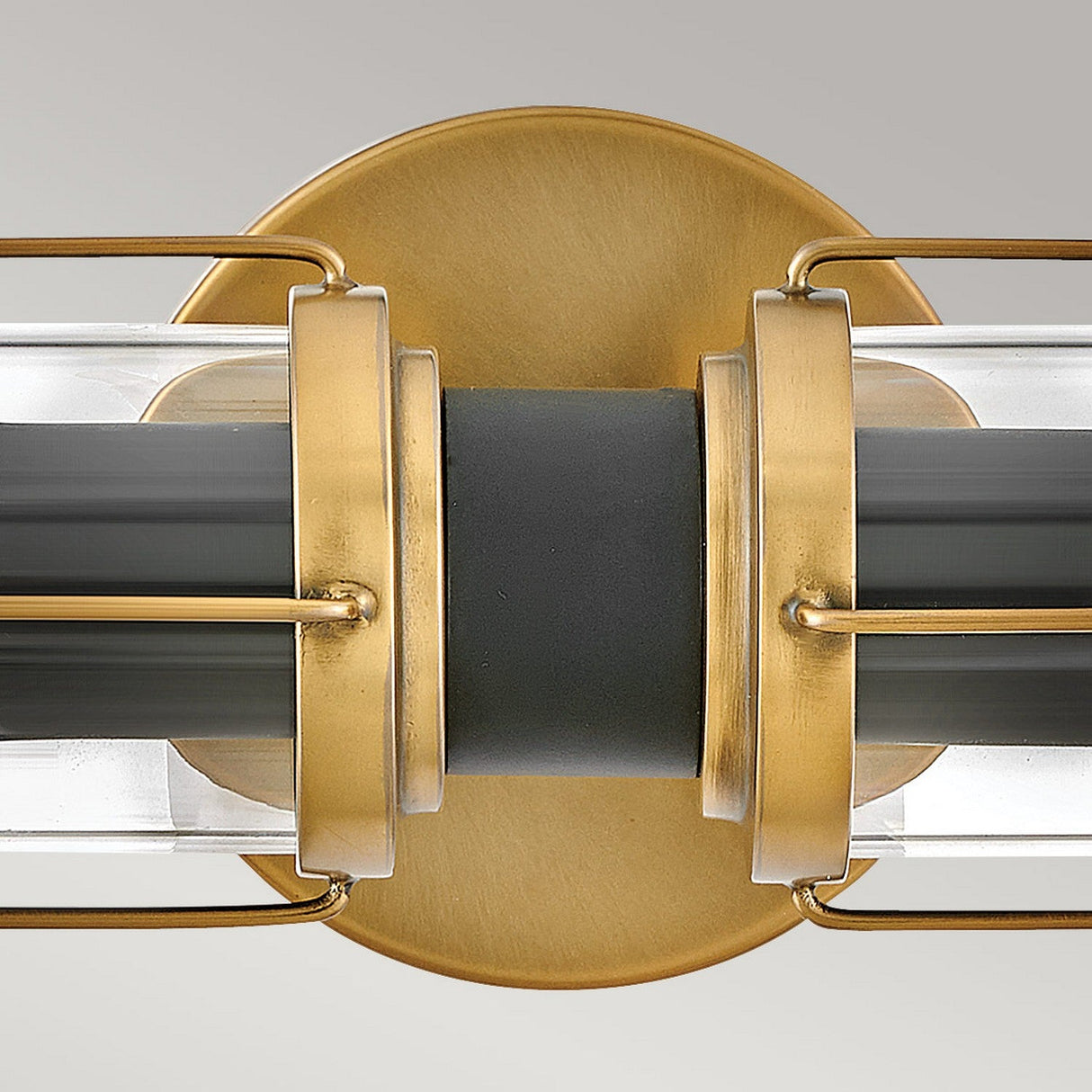 The Masthead 2 Light Wall Light features a close-up of its modern design, displaying clear glass shades with a black central section. The fixture is finished in Heritage Brass and complemented by a gold metal frame with a circular base, blending elegance with contemporary allure.