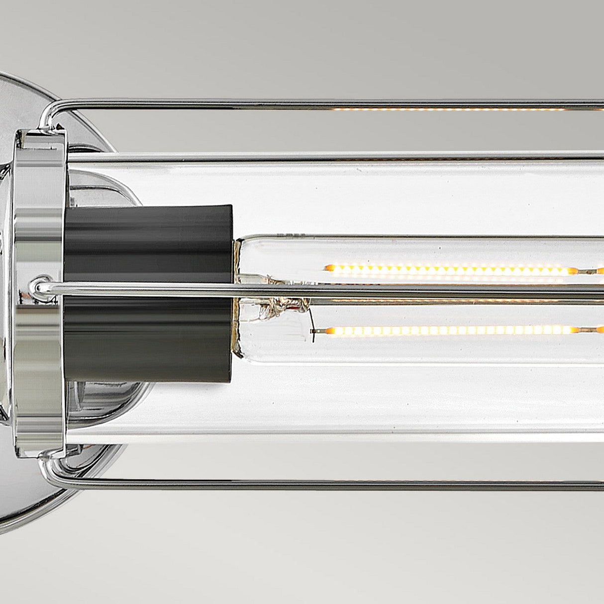 Close-up of the Masthead 2 Light Wall Light - Polished Chrome & Black, showcasing a cylindrical glass shade. The fixture offers a touch of nautical charm with its polished chrome accents and visible LED filaments, set against a plain gray background.