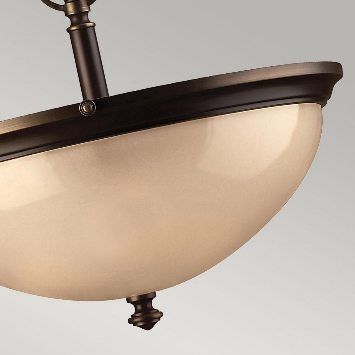 Close-up of the Mayflower 3 Light Pendant - Bronze, showcasing a bronze and frosted glass semi-flush ceiling light fixture with an adjustable height. It features a shallow dome shape, a metal rim, and a decorative finial at the bottom, all set against a light gray background.