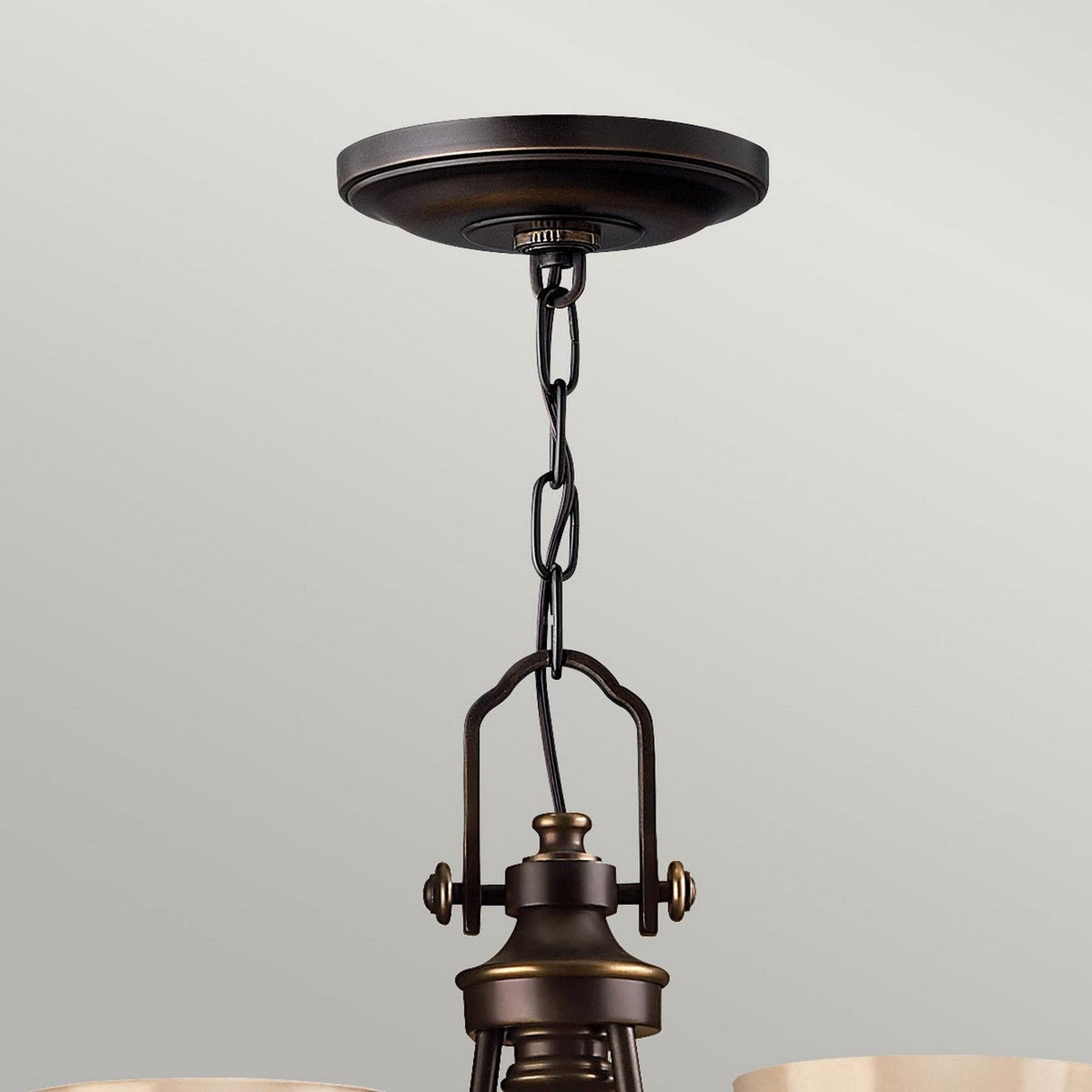 The Mayflower 3 Light Chandelier, featuring a ceiling-mounted design, exudes traditional elegance with its dark bronze canopy. The fixture's metal body is supported by a chain, while etched amber glass gently diffuses the light against a neutral, light gray background.