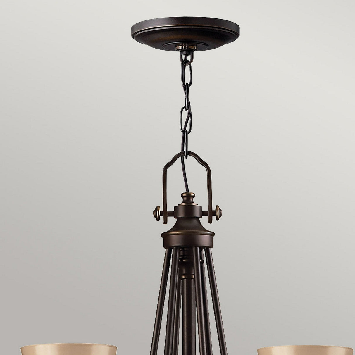 Close-up of the Mayflower 9 Light Chandelier - Bronze, showcasing its elegant design with a chain suspension from a ceiling mount, a central rod, and intricately etched amber glass shades. This chandelier artfully combines modern and classic styles against a plain gray background.