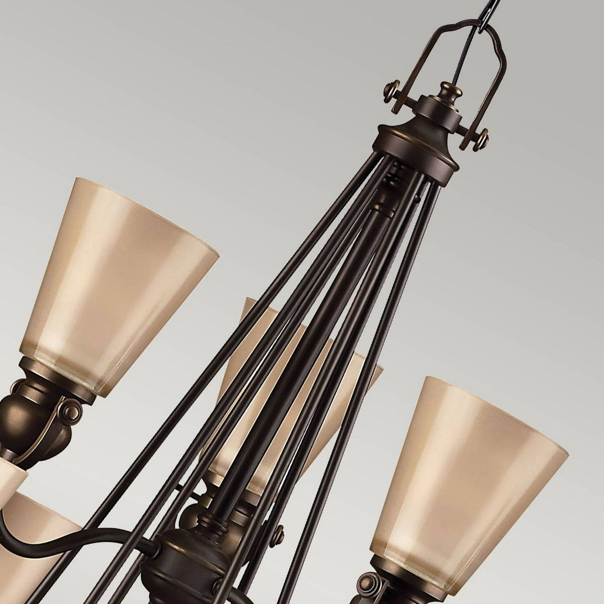 Close-up of the Mayflower 9 Light Chandelier - Bronze, showcasing multiple upward-facing beige lampshades. The chandelier features intricate metalwork with slender rods converging at the top. Its elegant design is highlighted against a plain light gray background.