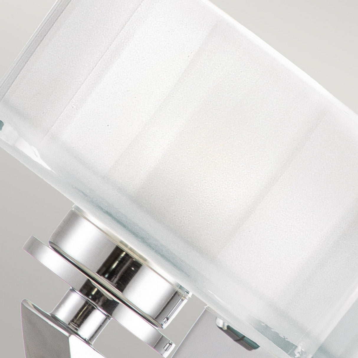 A close-up of the Meridian 1 Light Wall Light - Polished Chrome showcases its modern elegance with a frosted glass shade and a sleek metallic base. The lamp is angled slightly to the right against a neutral background, its polished chrome finish enhancing its contemporary appeal.