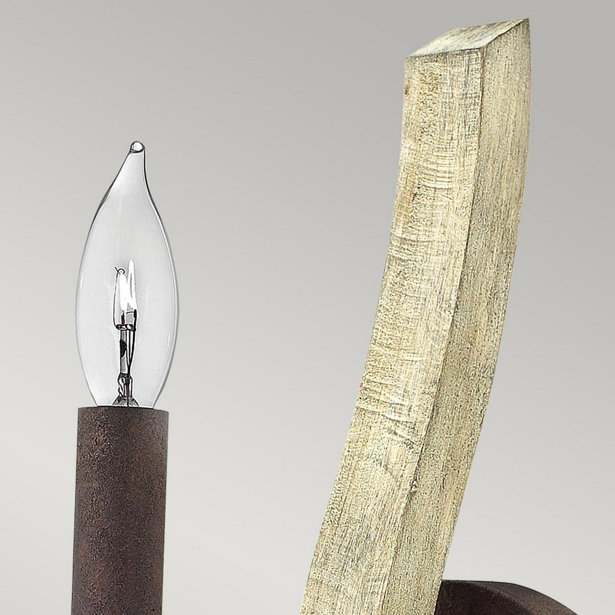 Close-up of the Middlefield 1 Light Wall Light in Iron Rust, a candle-shaped bulb fixture on a rustic, curved wooden and metal lamp, showcasing industrial style with a textured finish against a plain gray background.