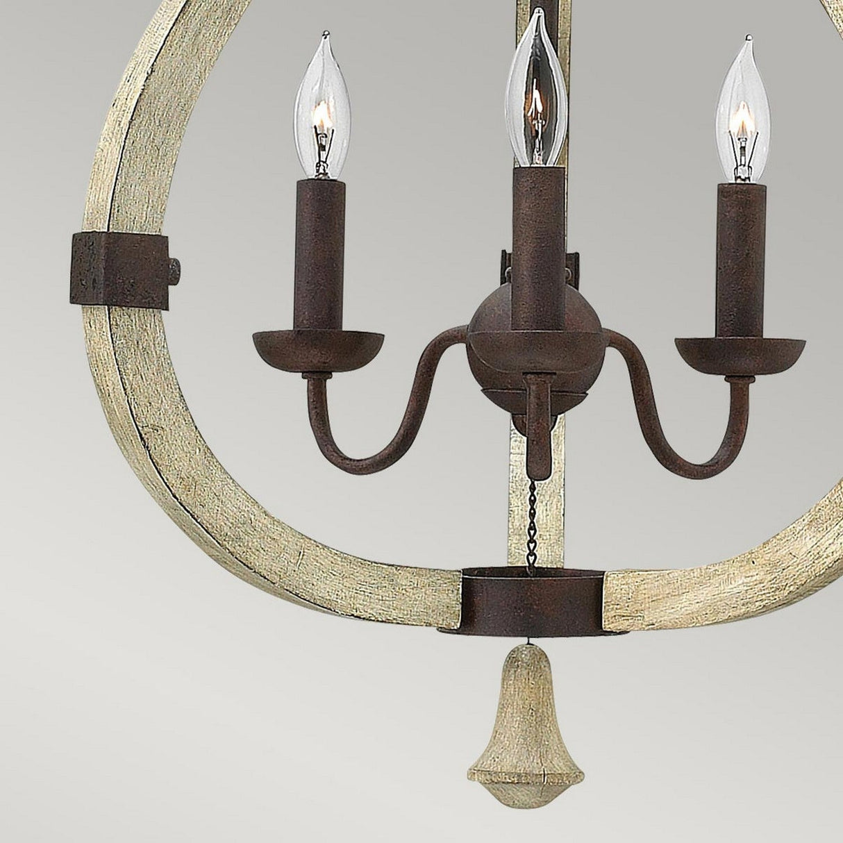 A close-up of the Middlefield 3 Light Chandelier - Iron Rust, showcasing its three candle-like light bulbs, dark brown metal arms with an iron rust finish, and a circular distressed wood frame, set against a neutral gray background.