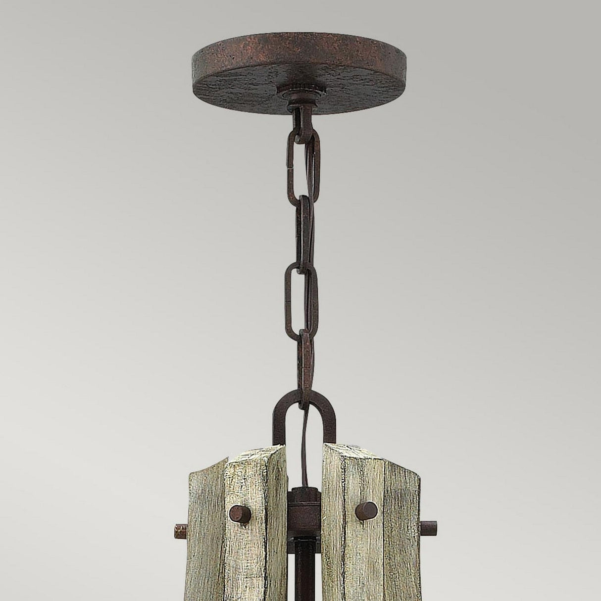 The Middlefield 6 Light Chandelier - Iron Rust showcases a rustic design with a round metal ceiling mount, chain link for hanging, and distressed wood featuring iron rust finish accents at the base. The simple gray backdrop enhances its vintage charm.