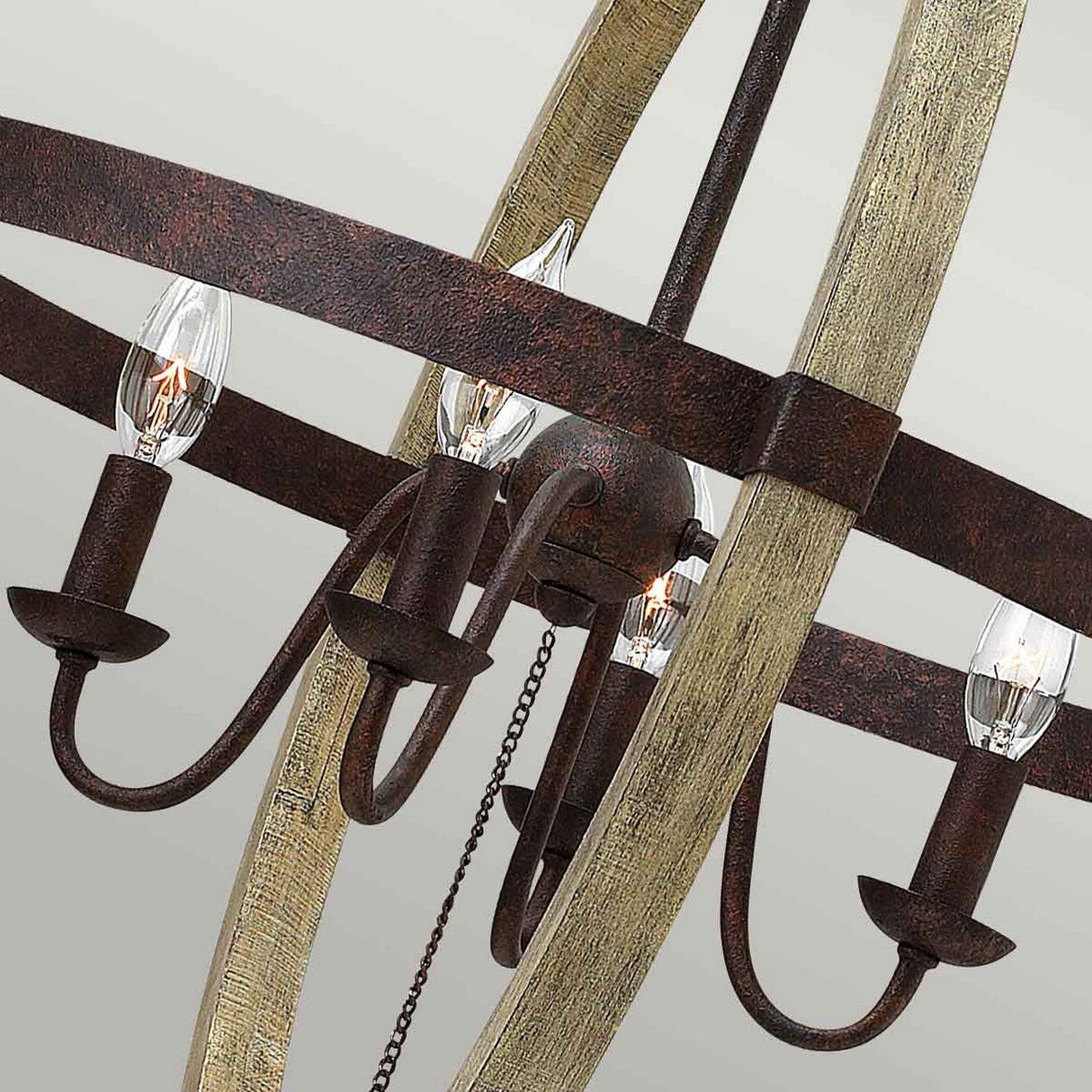 The Middlefield 4 Light Chandelier - Iron Rust showcases a rustic elegance with its ornate design. It features curved dark iron rust tone arms that hold exposed candle-shaped light bulbs. The chandelier's antique finish is beautifully accented with distressed wood elements, giving it an elegant and vintage appearance.