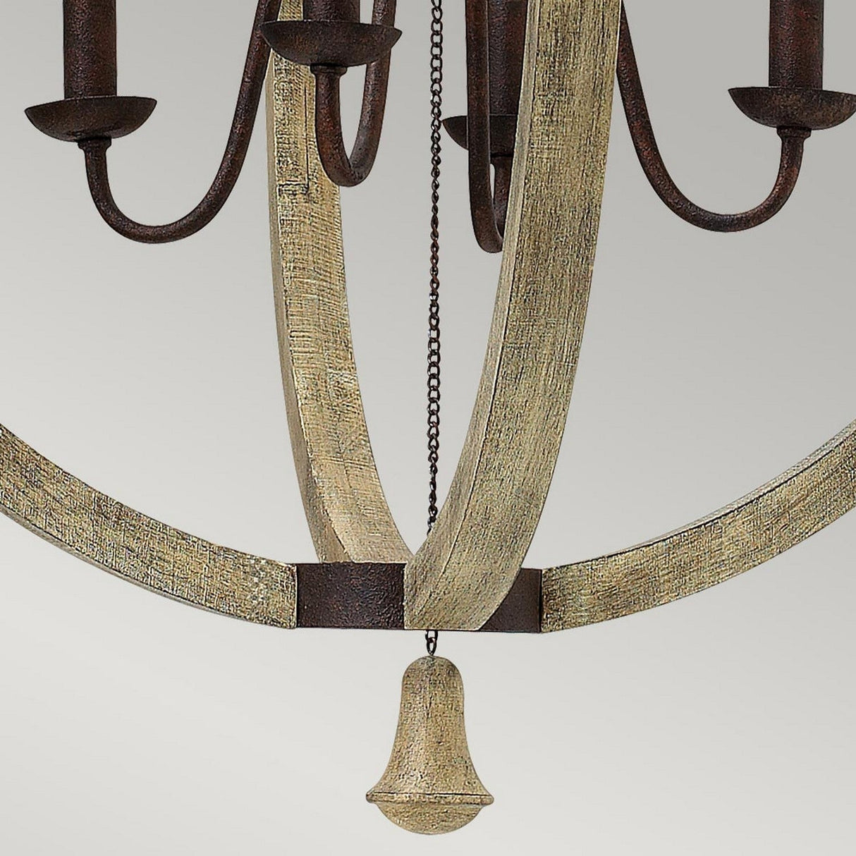 A close-up of the Middlefield 4 Light Chandelier showcases its elegant charm with gracefully curved metal arms in an iron rust tone and a distressed, textured finish. A chain descends elegantly, culminating in a bell-shaped ornament against a simple light gray background.