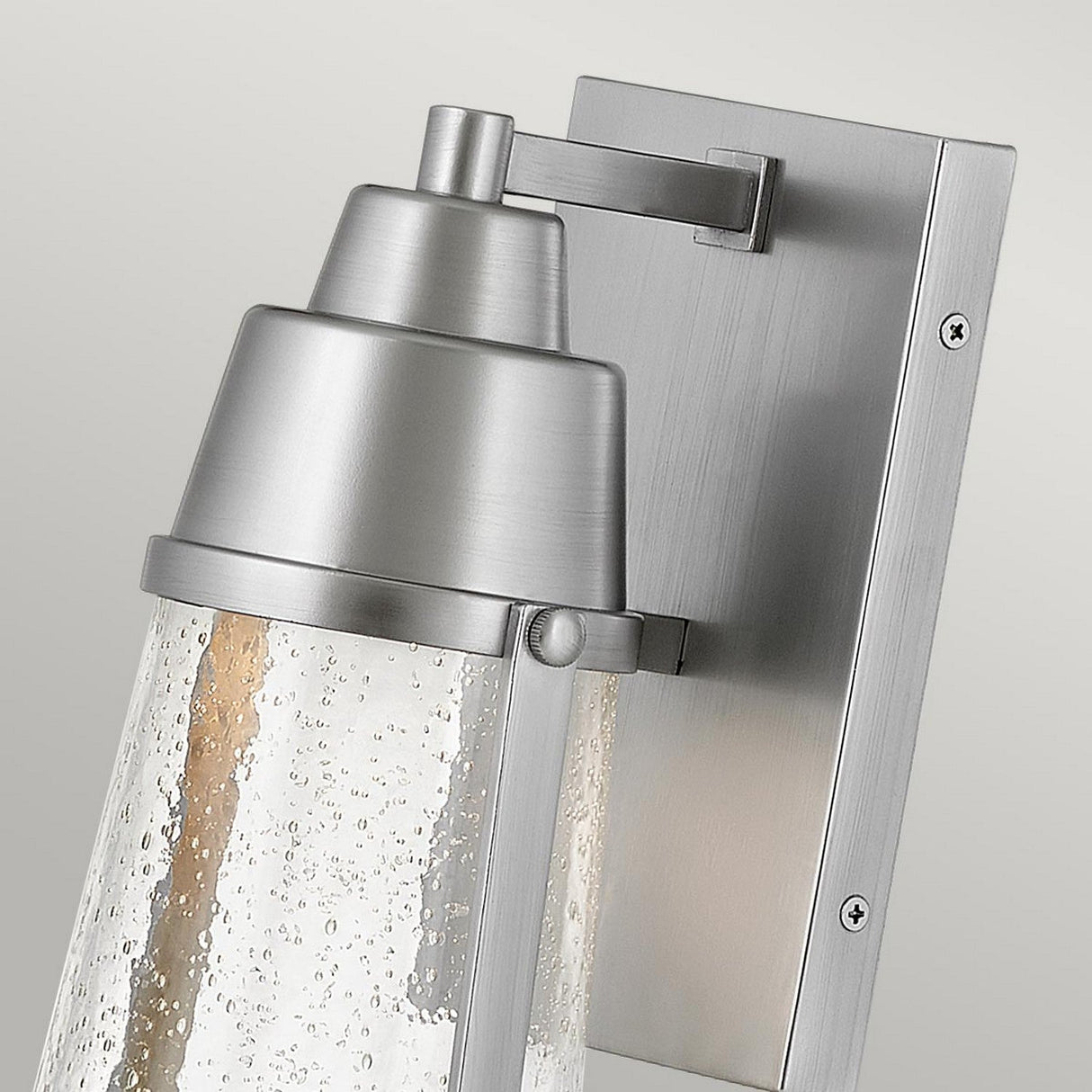 Introducing the Miles 1 Light Wall Lantern in Painted Satin Nickel, a contemporary wall sconce featuring a brushed metal finish and a textured glass shade. Equipped with an LED GU10 lamp, this fixture is mounted on a rectangular metal backplate and exudes a sleek design with subtle nautical charm.