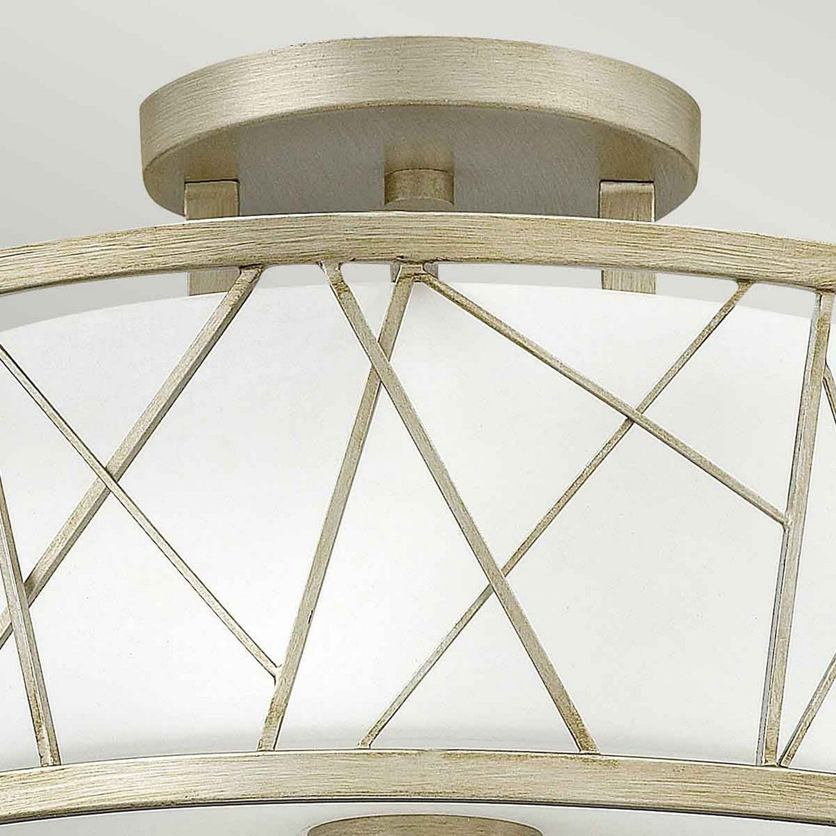 Close-up of the Nest 3 Light Semi Flush, an organic modern ceiling light with criss-crossing metal bars in a lustrous gold finish over a linen glass shade. The circular base perfectly complements its geometric pattern.