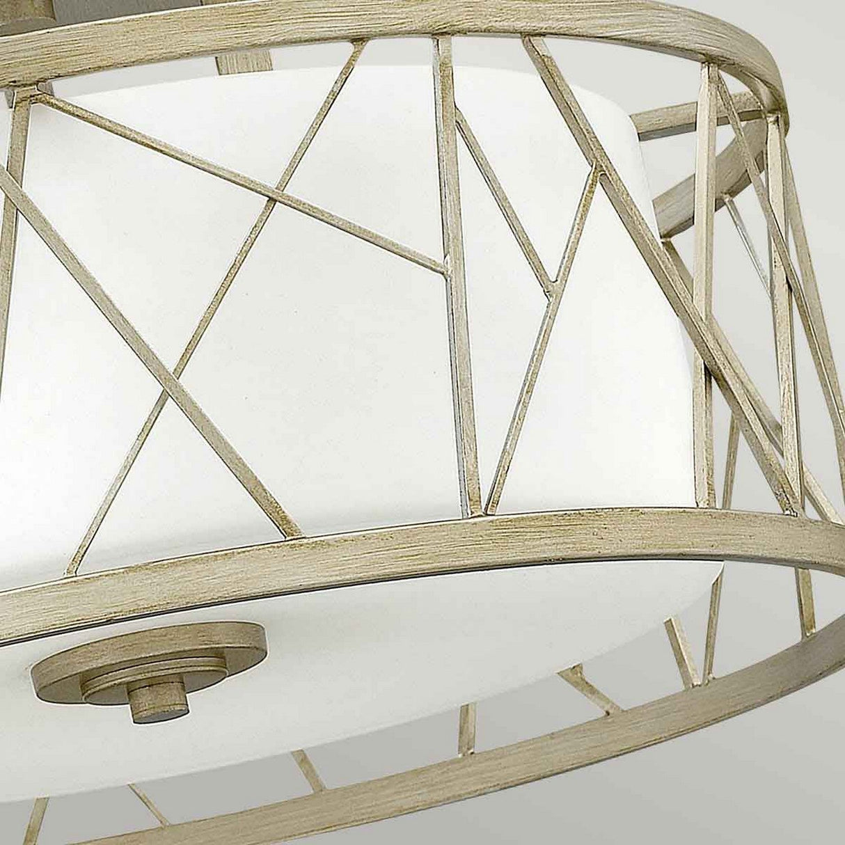 A close-up of the Nest 3 Light Semi Flush fixture showcases its modern, organic design with an elegant gold crisscross metal frame. This intricate pattern encircles a white linen glass shade, enhancing the geometric aesthetic that perfectly aligns with a sophisticated style.