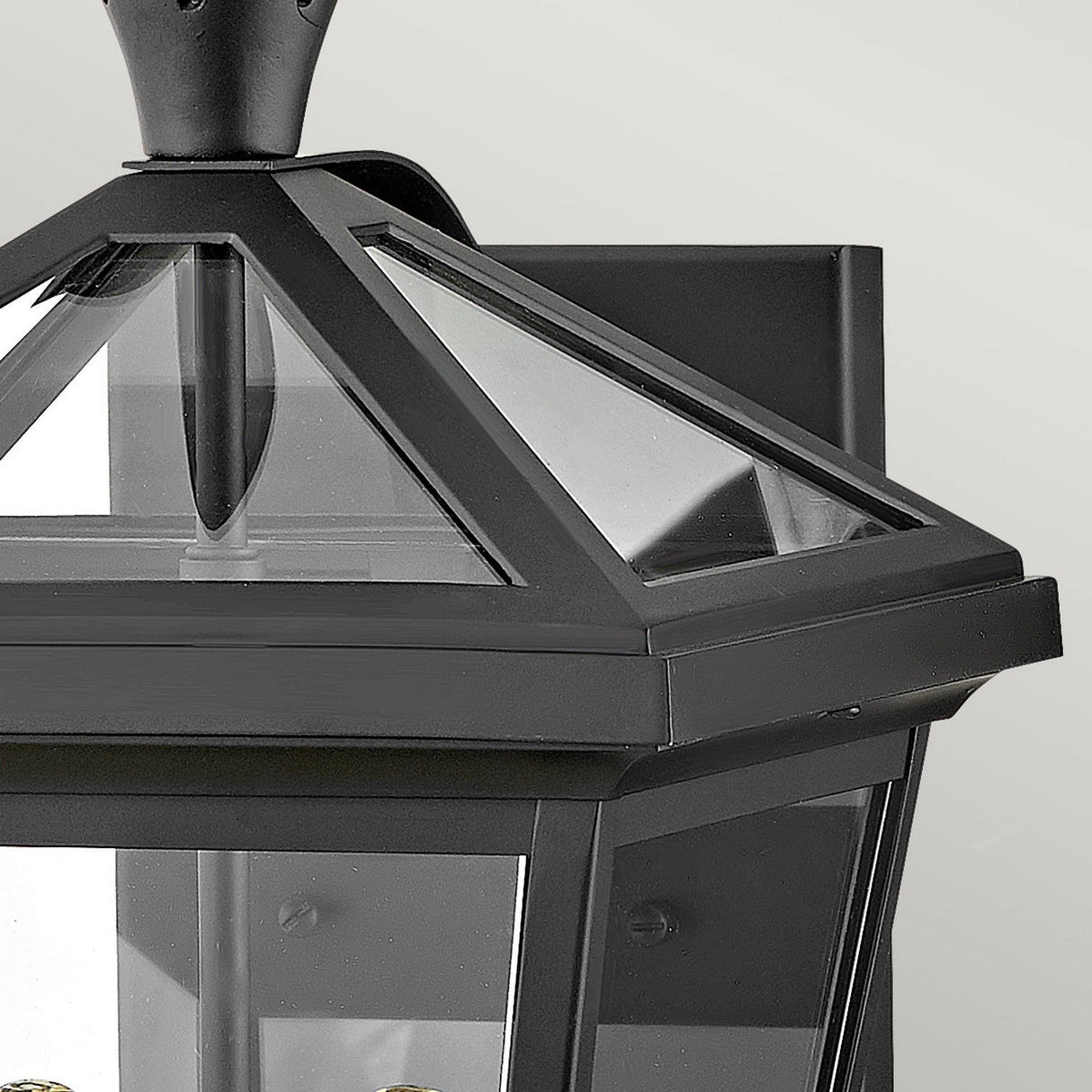 Close-up of the Palma Outdoor 2 Light Medium Wall Lantern in black, featuring a pyramid-shaped glass top and clear panels. This elegant lantern showcases a subtle pineapple motif, emphasizing its simple yet modern geometric design against a plain background.
