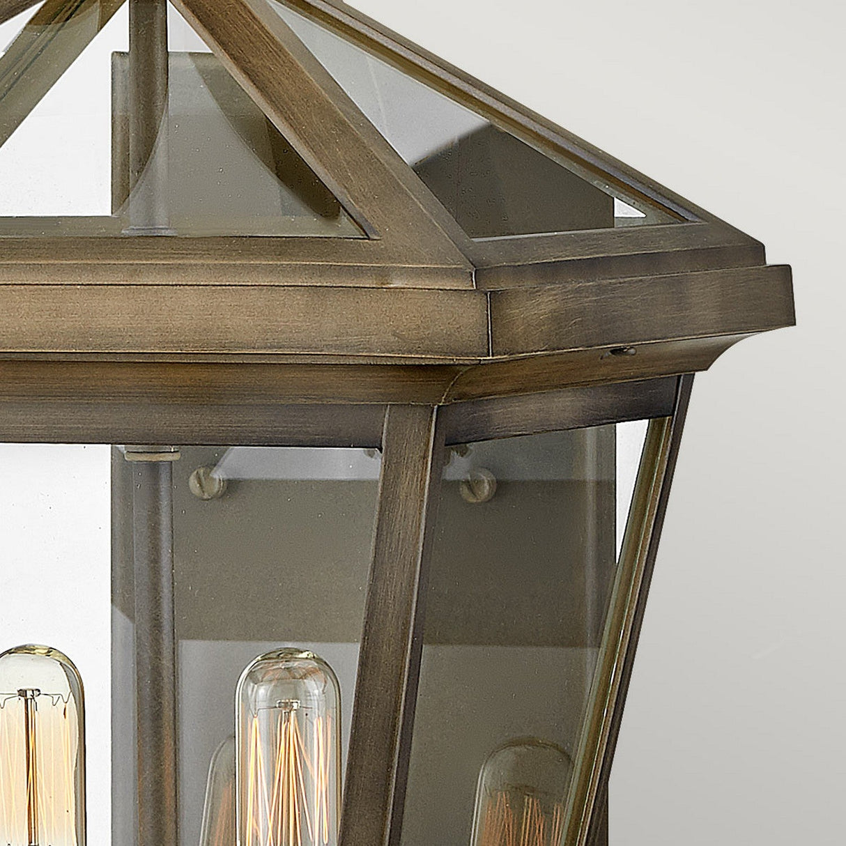 Introducing the Palma Outdoor 2 Light Medium Wall Lantern in Burnished Bronze, showcasing a geometric design with clear glass panels and exposed vintage-style bulbs. This lantern seamlessly merges a modern and classic aesthetic, making it ideal for outdoor decor.
