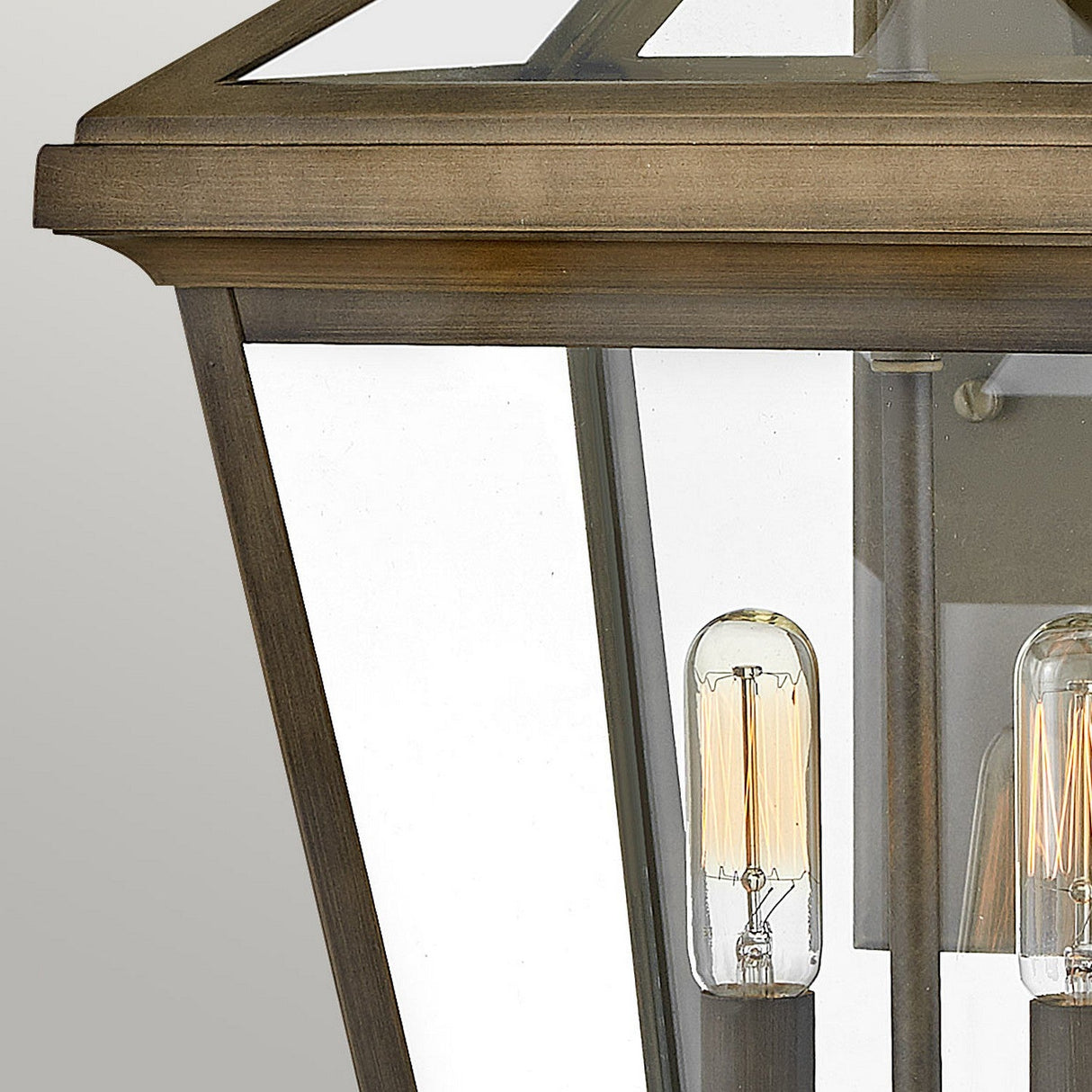 A close-up of the Palma Outdoor 2 Light Medium Wall Lantern showcases its vintage style with clear glass panels and an exposed filament bulb. The lantern features a warm brass finish over burnished bronze and is wall-mounted, offering a classic and elegant touch to your outdoor decor.