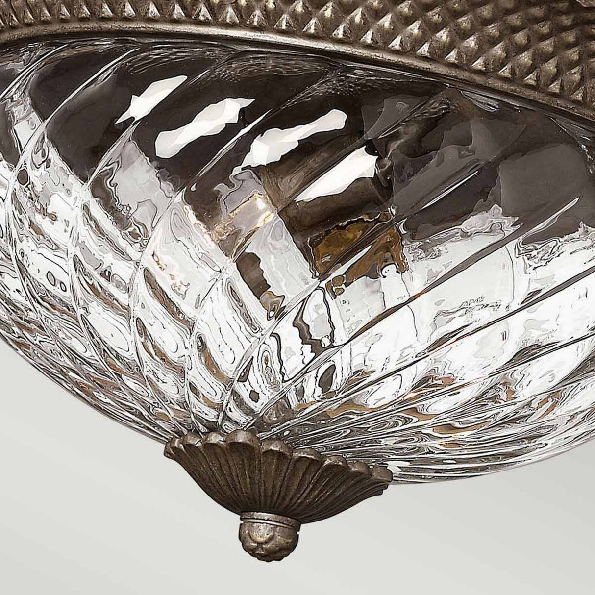 Get a closer look at the Plantation 3 Light Large Flush - Bronze, featuring an ornate swirling design and surrounded by a textured bronze flush mount. The handcrafted glass beautifully reflects light off its curved surface, offering an elegant and classic aesthetic.