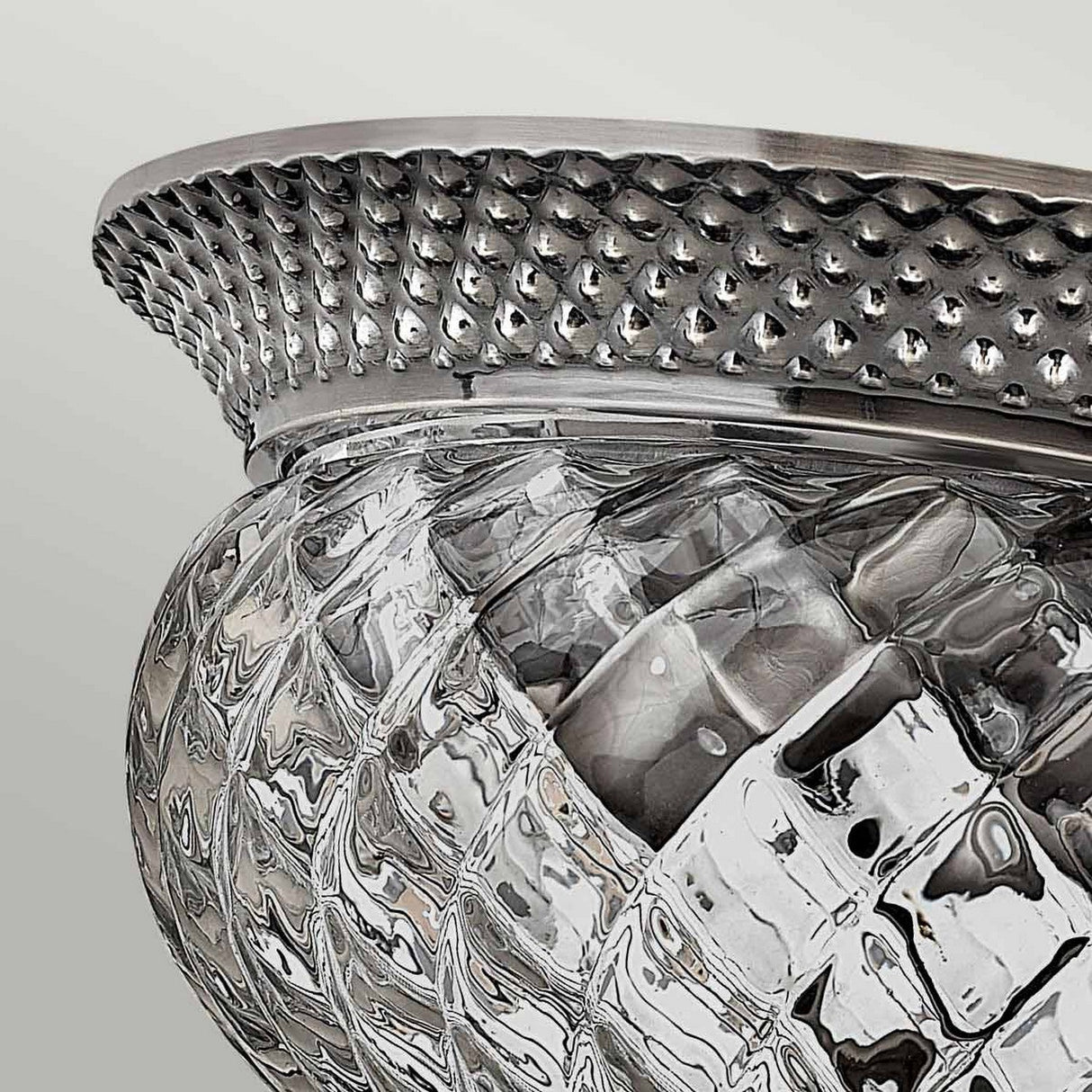 Close-up of the Plantation 2 Light Small Flush fixture in polished antique nickel, featuring a textured glass and metal design with a woven pattern. The metal rim showcases a dotted texture, while the optic glass below is intricately crafted with a diamond pattern. The background is a soft, neutral gray.