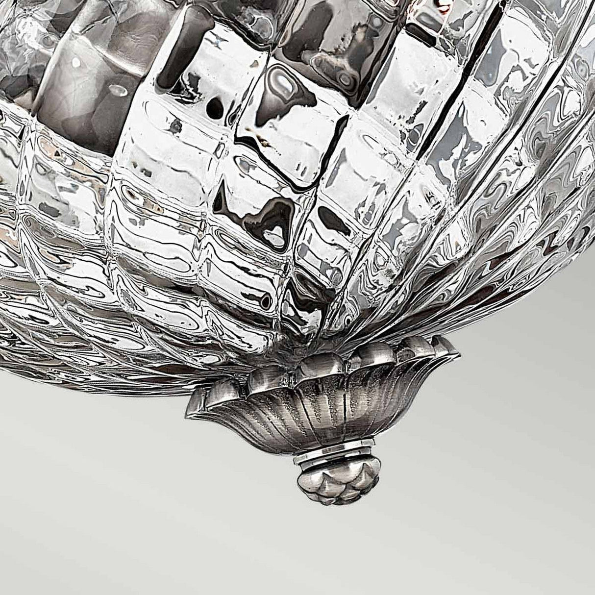 Close-up of the Plantation 2 Light Small Flush - Polished Antique Nickel, showcasing its silver decorative design with a textured, reflective surface resembling a faceted sphere. A delicate floral element accents the bottom, set against a plain, light-colored background that highlights its elegant charm.