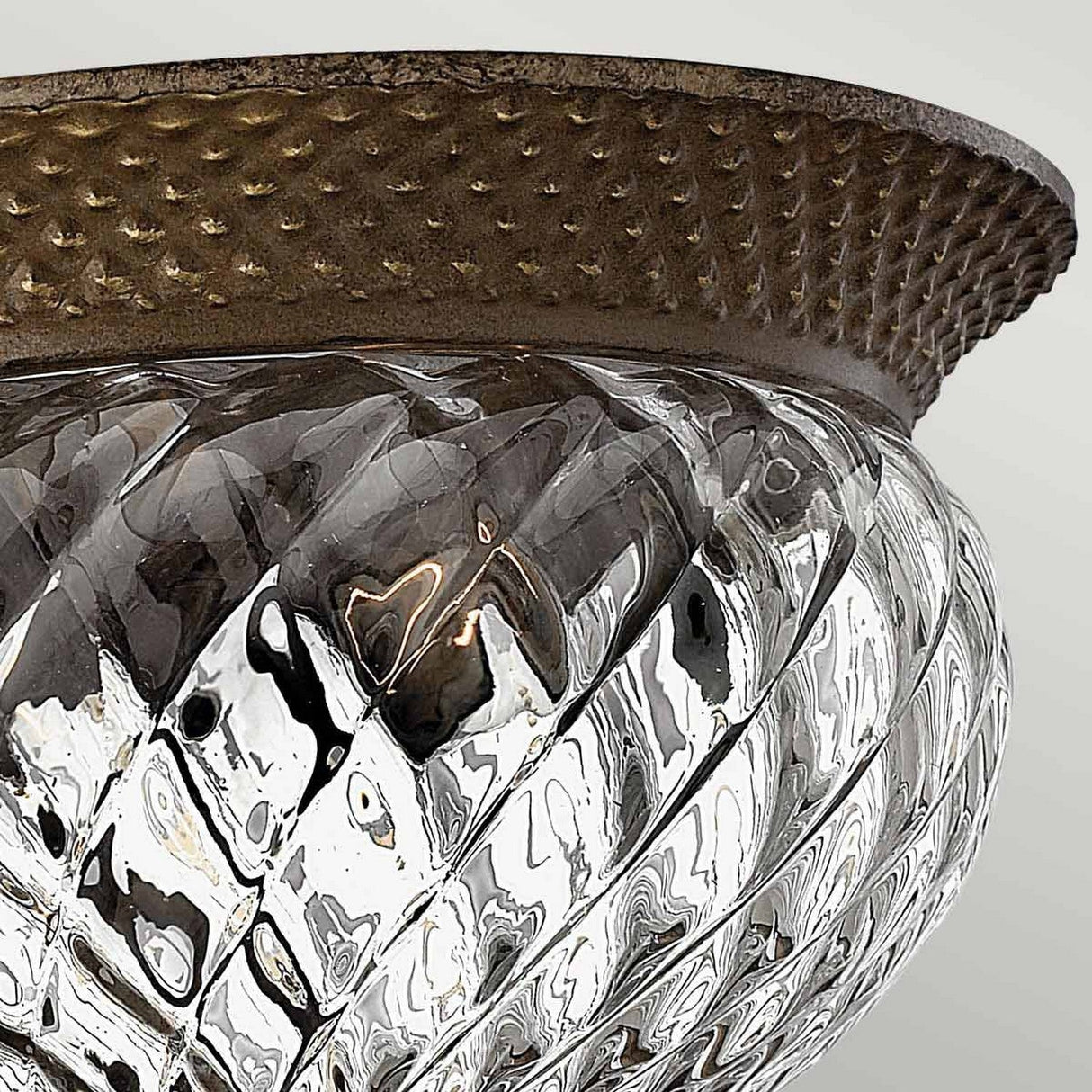 Close-up of the Plantation 2 Light Small Flush - Bronze, showcasing its textured, diamond-patterned optic glass shade and a decorative metal rim finished in bronze. The pattern creates a reflective effect with soft lighting visible inside, while the dot pattern on the metal rim adds intricate detail to the design.