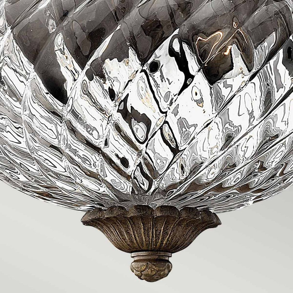 Close-up of a decorative glass chandelier featuring swirling patterns and a metallic floral base with a bronze finish. The optic glass’s reflective, textured surface produces an elegant, artistic effect, reminiscent of the Plantation 2 Light Small Flush - Bronze design.