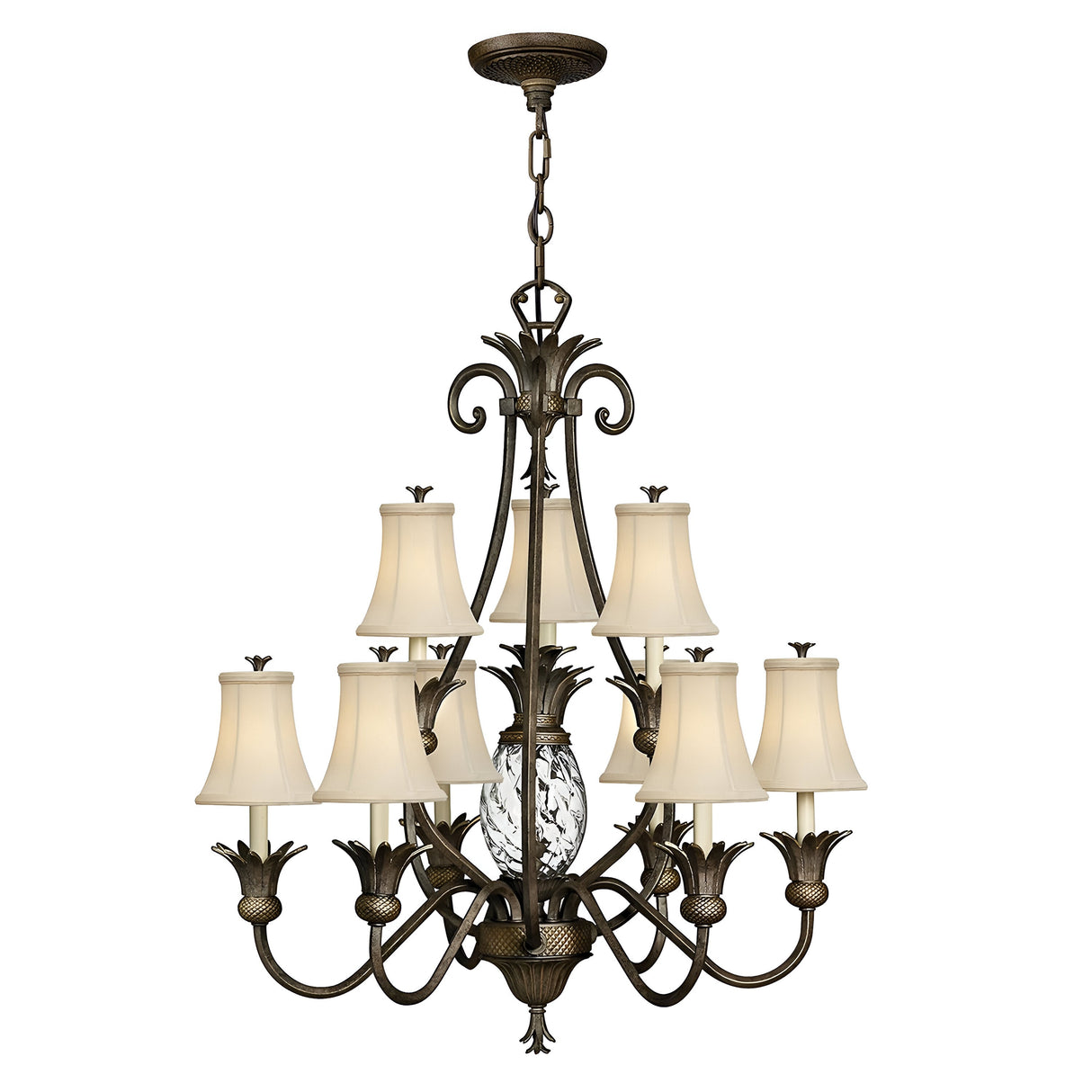 The Plantation 10 Light Chandelier in bronze is a large, ornate fixture featuring decorative cast detailing. It includes multiple curved arms and ten cream-colored lampshades arranged in tiers, with a pineapple-shaped glass centerpiece enhancing its elegant design.