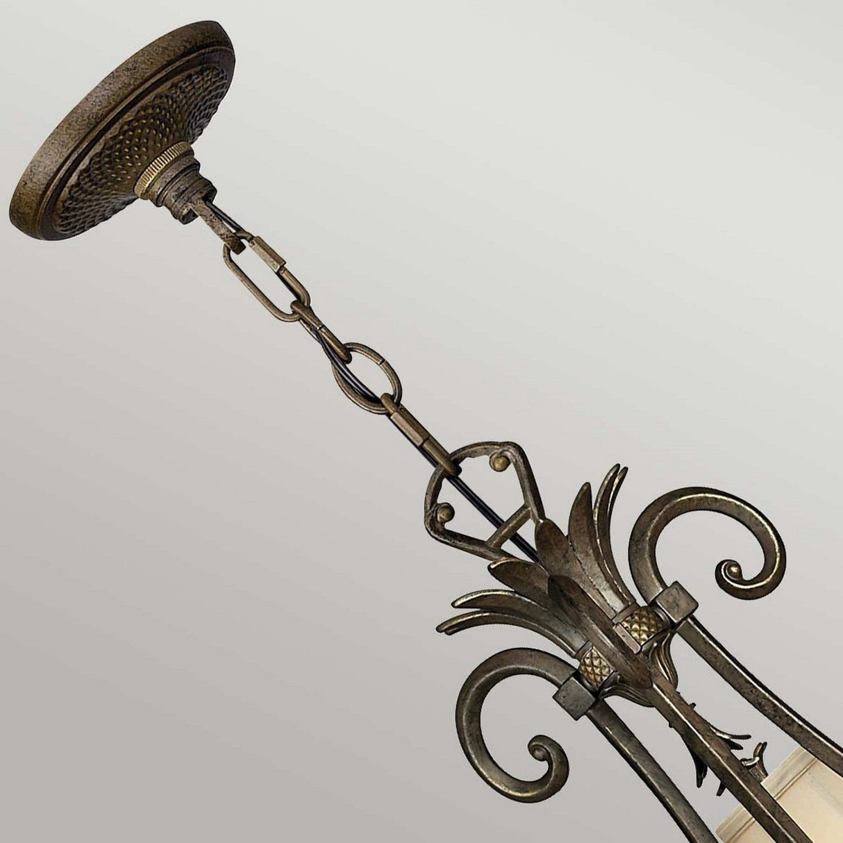 The Plantation 10 Light Chandelier in bronze showcases a decorative design with ornate scrollwork, pineapple-shaped glass accents, and chain link details set against a plain background.