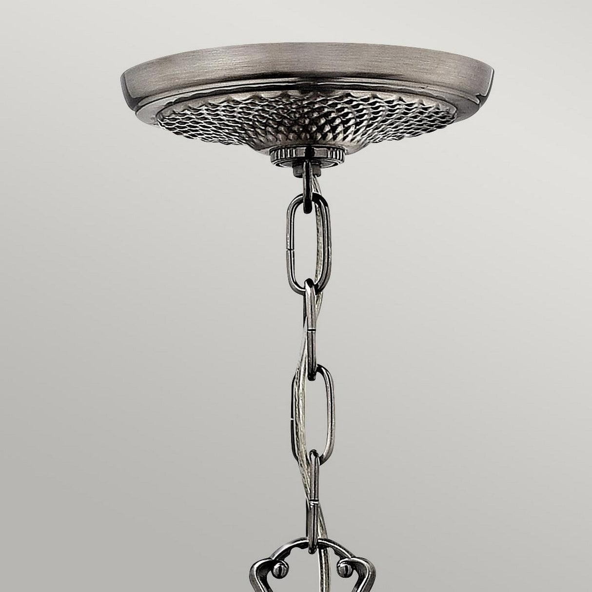 Close-up of a ceiling mount for a hanging light fixture with a textured metal base and linked chain. The Plantation 3 Light Chandelier - Polished Antique Nickel features a smooth, reflective surface that elegantly contrasts against the plain, light gray background.