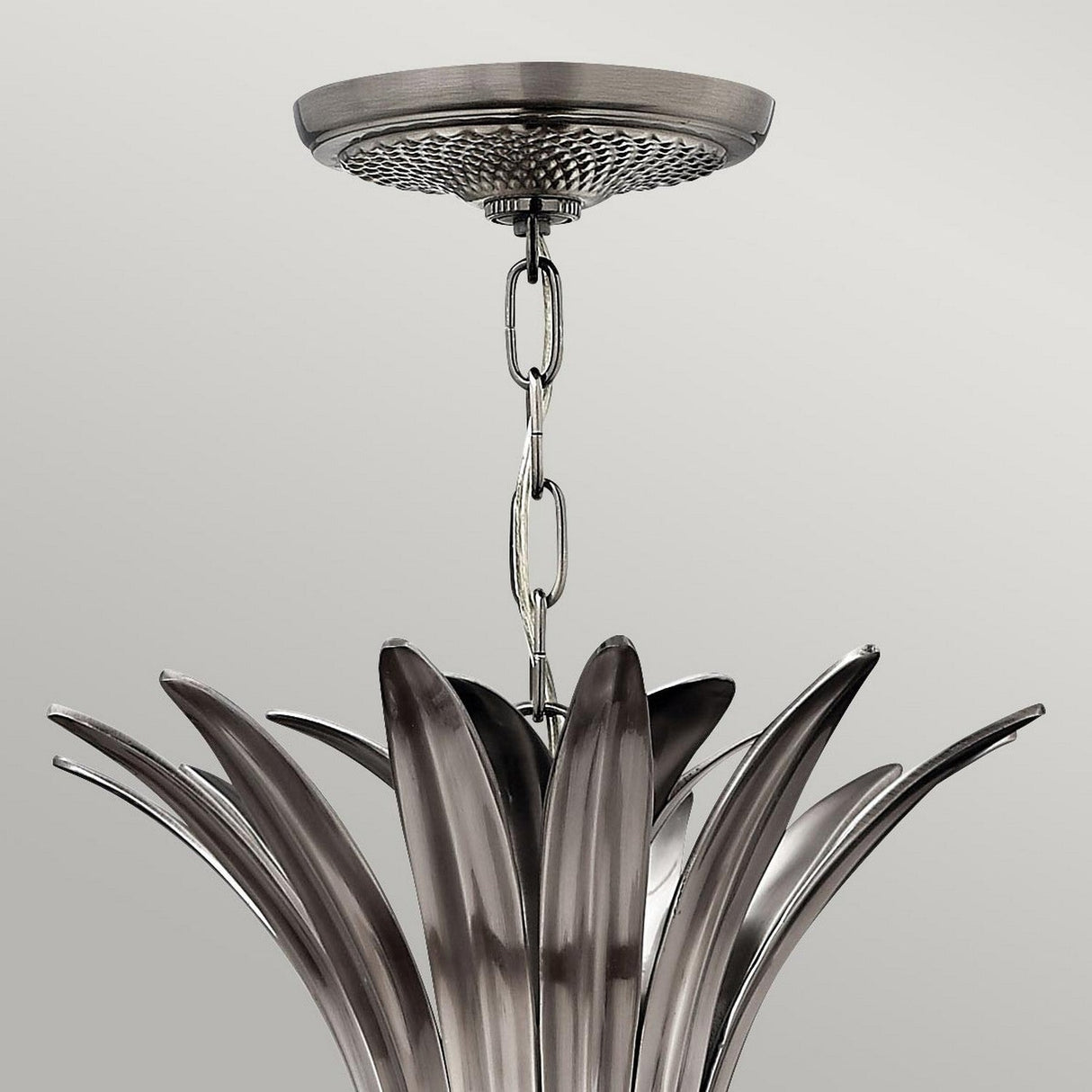 A close-up shot of a metallic light fixture with petal-like elements and a polished antique nickel finish, suspended from a chain. This sleek, modern design is reminiscent of the Plantation 4 Light Pendant - Polished Antique Nickel and is mounted on a round base attached to the ceiling, against a plain light gray background.