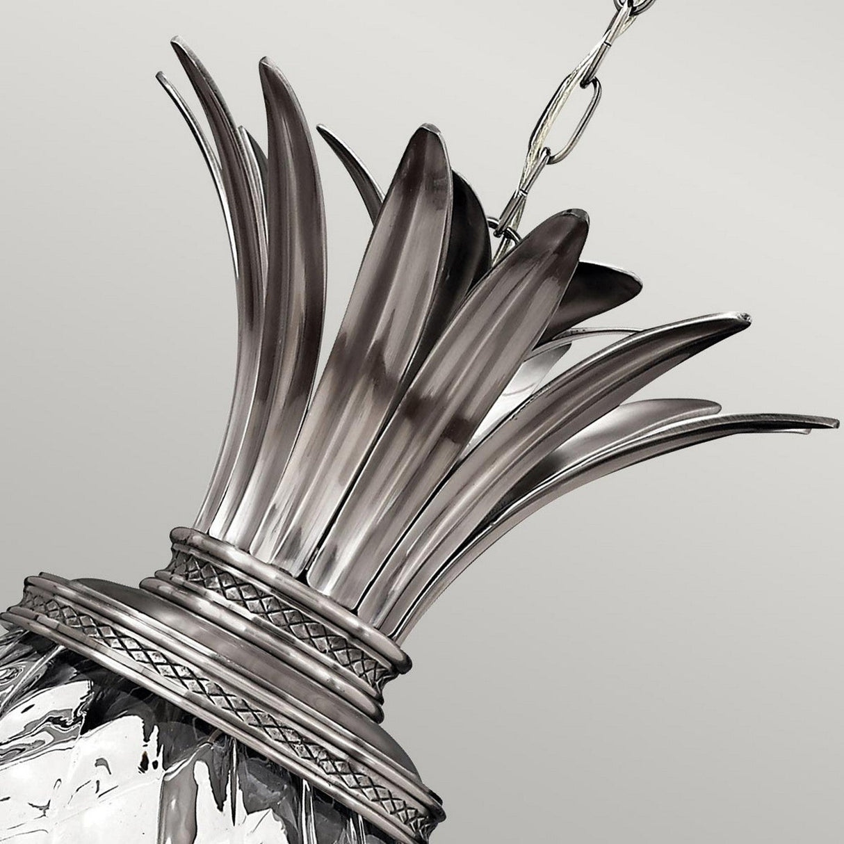 Close-up of the Plantation 4 Light Pendant in polished antique nickel, featuring a decorative metallic pineapple shape. The top displays elongated leaves, and the body boasts an intricate, textured surface with a shiny finish. It hangs gracefully from a chain against a neutral background.