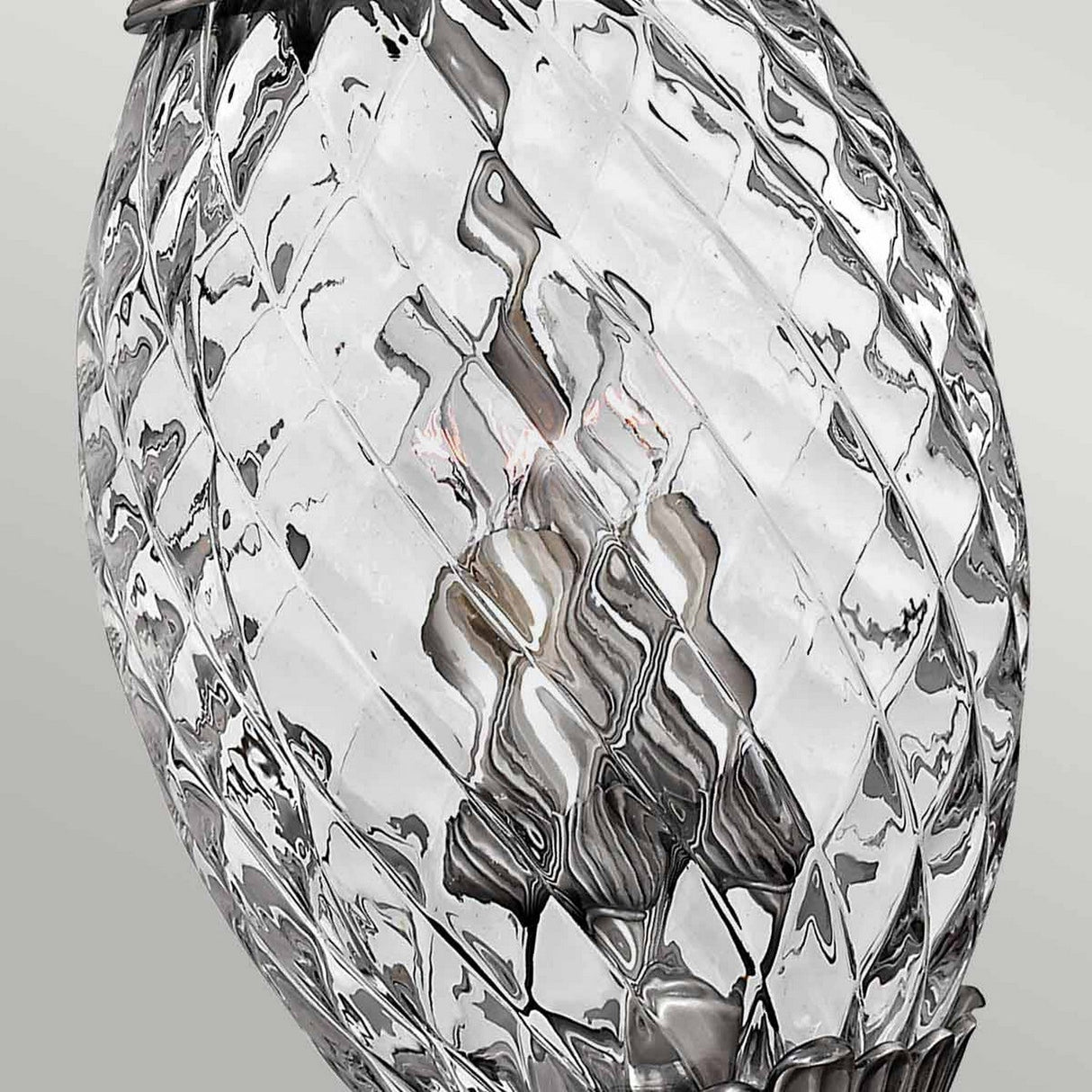 A close-up view of the Plantation 4 Light Pendant in Polished Antique Nickel showcases its textured, pineapple-shaped clear optic glass design, encasing a bulb inside. The reflective glass surface distorts the view of the bulb and fixtures, while a plain, light-colored background elegantly complements the polished antique nickel accents.